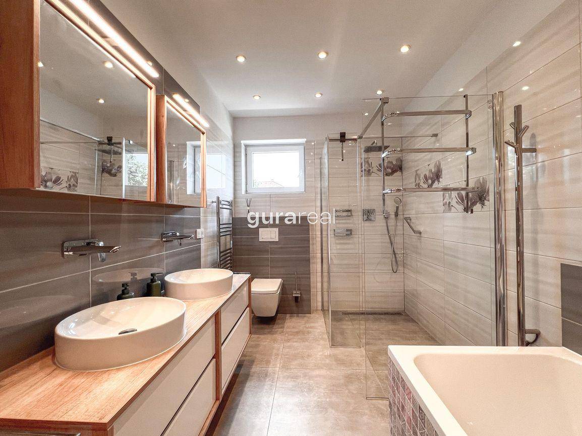 Geräumiges Badezimmer mit Doppelwaschbecken, großer Dusche und Badewanne am Fenster.