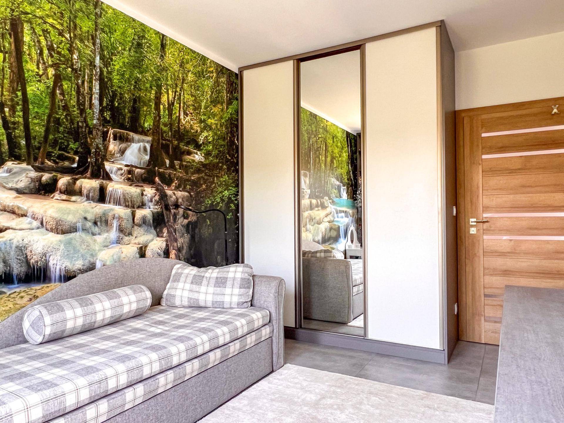 Schlafzimmer mit Tagesbett, integriertem Kleiderschrank und Wandtapete mit Naturmotiv.