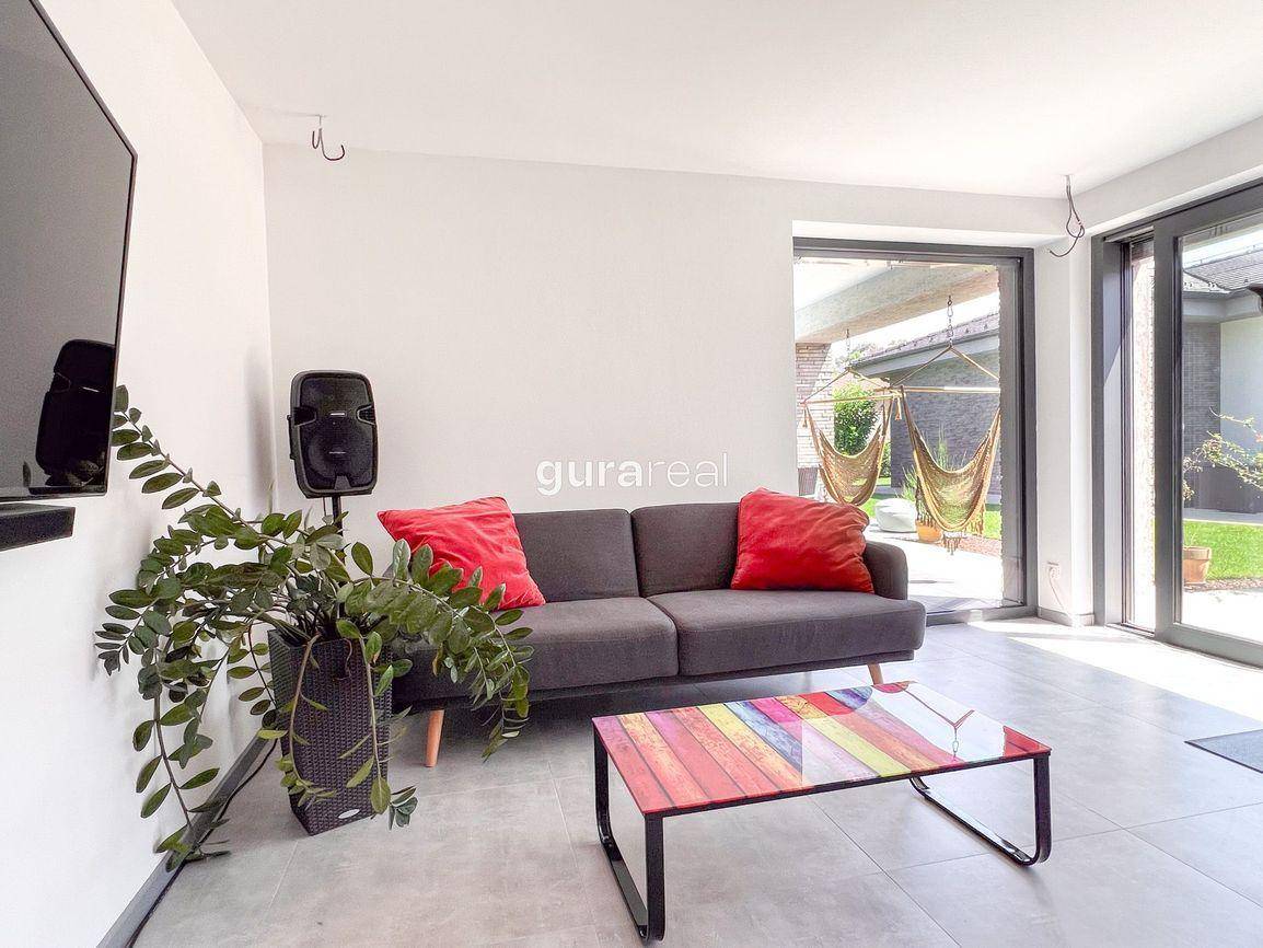 Helles Wohnzimmer mit modernem Sofa, großem Fenster und Zugang zum Außenbereich.