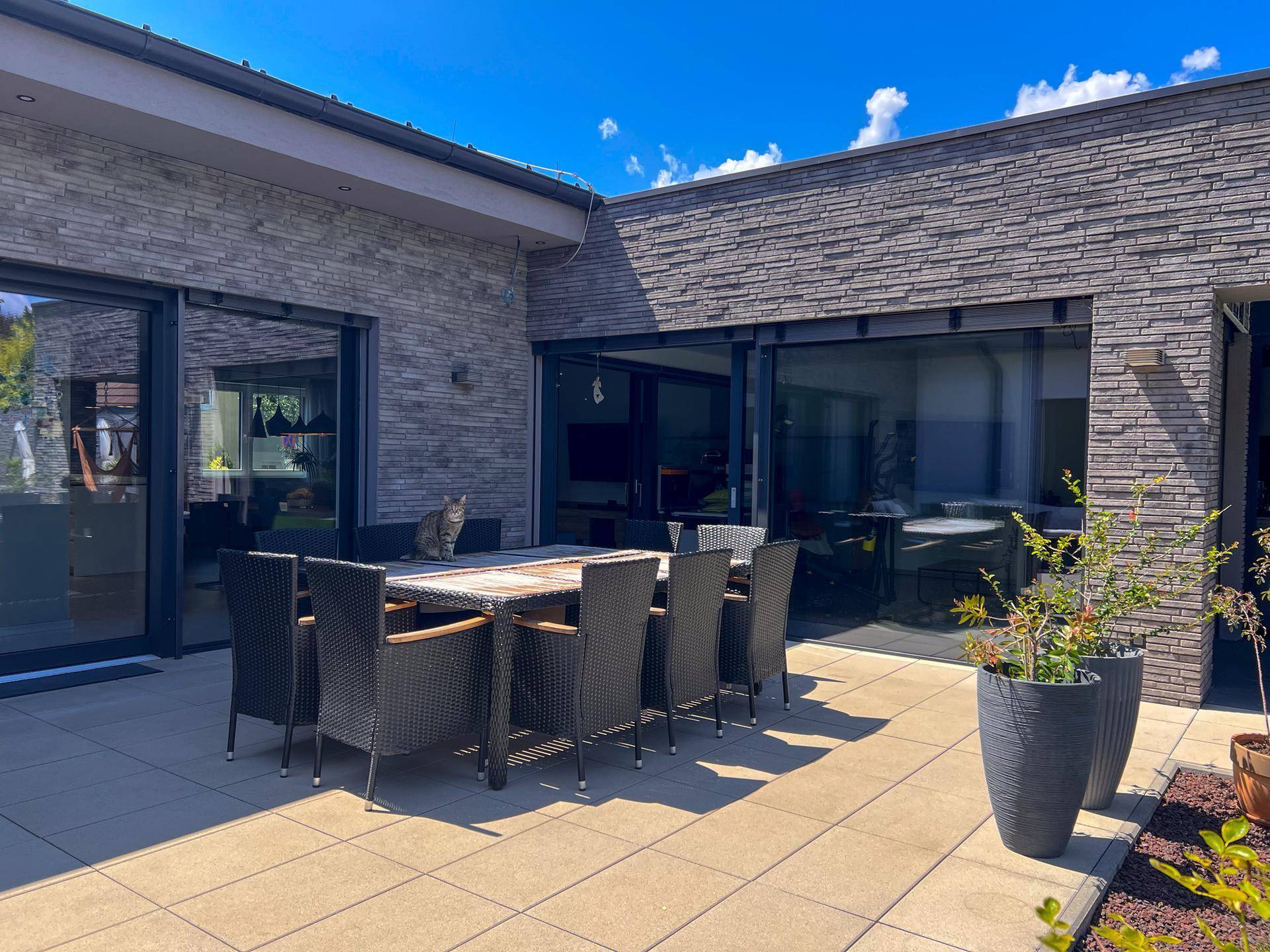 Große, sonnige Terrasse mit Esstisch und Stühlen, umgeben von moderner Architektur.
