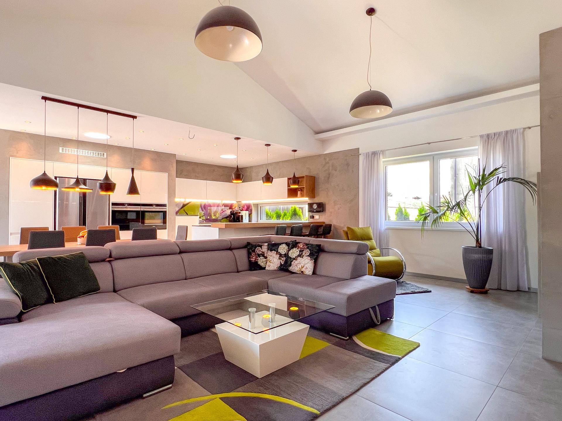 Offener Wohn-Essbereich mit moderner Küche, großem Sofa und hohen Decken.