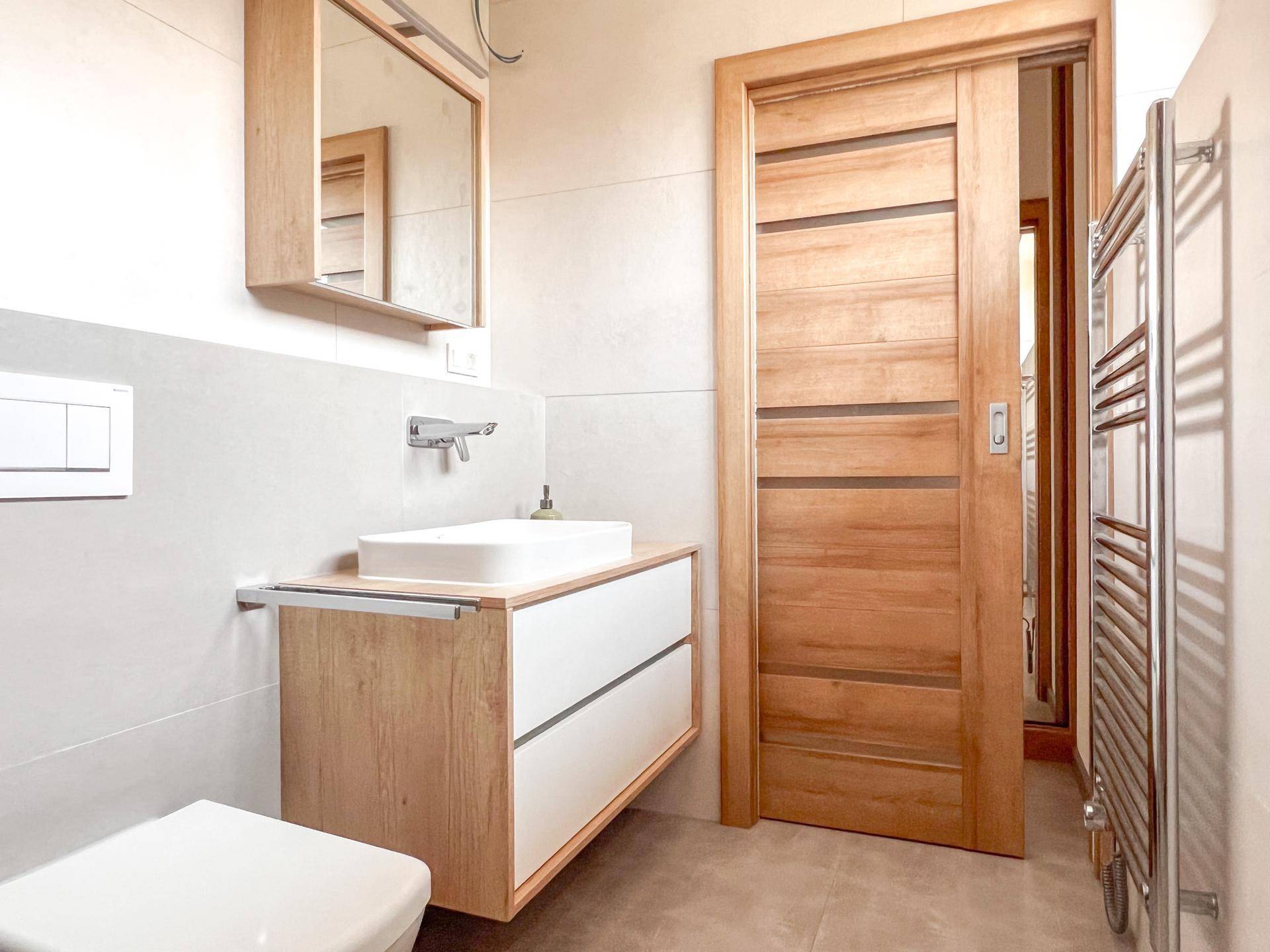 Modernes Badezimmer mit Waschtisch, Spiegel und Schiebetür aus Holz.