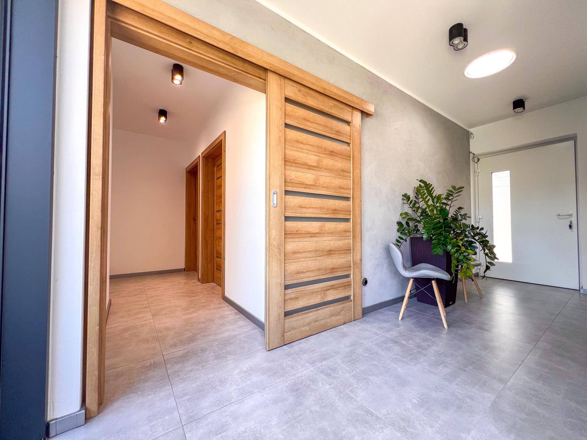 Heller Flur mit modernen Schiebetüren aus Holz und grauen Bodenfliesen.