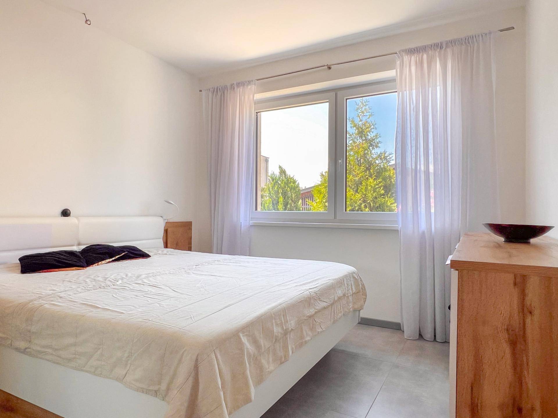 Helles Schlafzimmer mit Doppelbett, Holzmöbeln und großem Fenster.