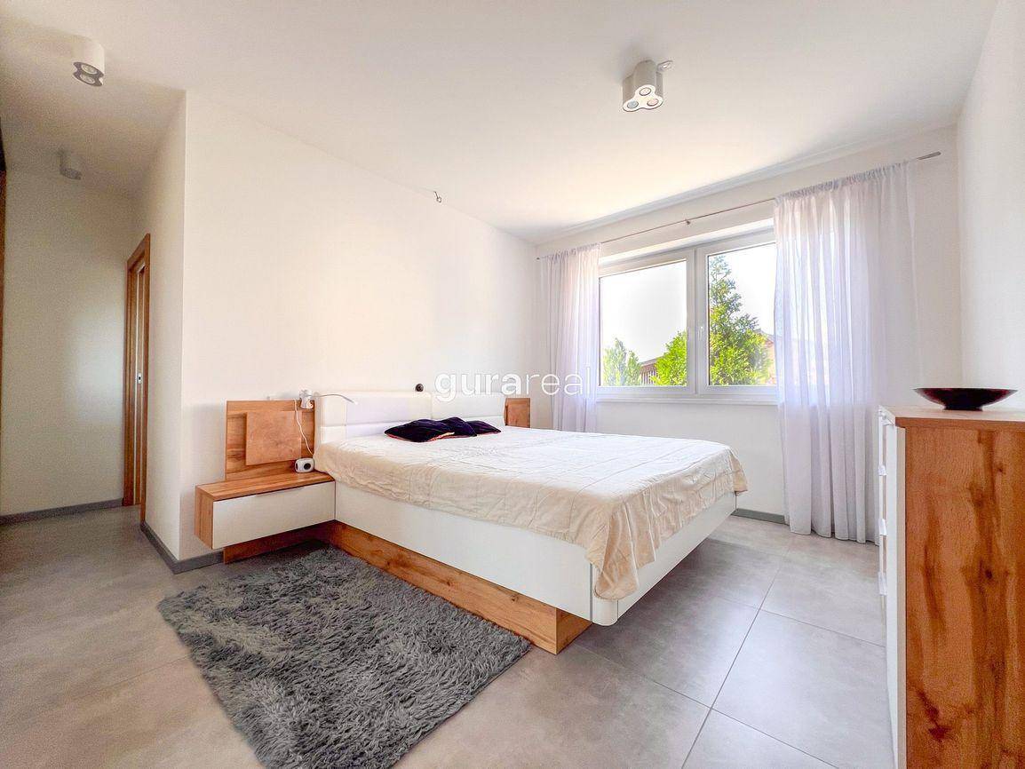 Helles Schlafzimmer mit modernem Bett, Holzmöbeln und großem Fenster mit Vorhängen.