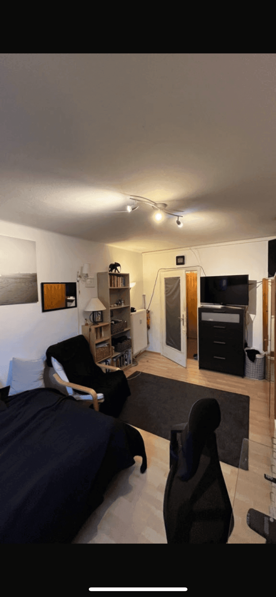 Gemütliches Schlafzimmer mit Holzboden, Regal und Fernseher, bietet eine entspannte Atmosphäre.