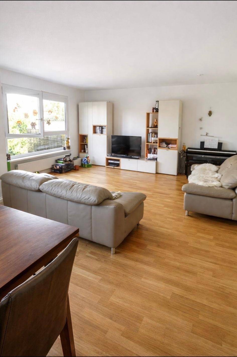 Helles Wohnzimmer mit Parkettboden, beigen Sofas und einem Klavier.