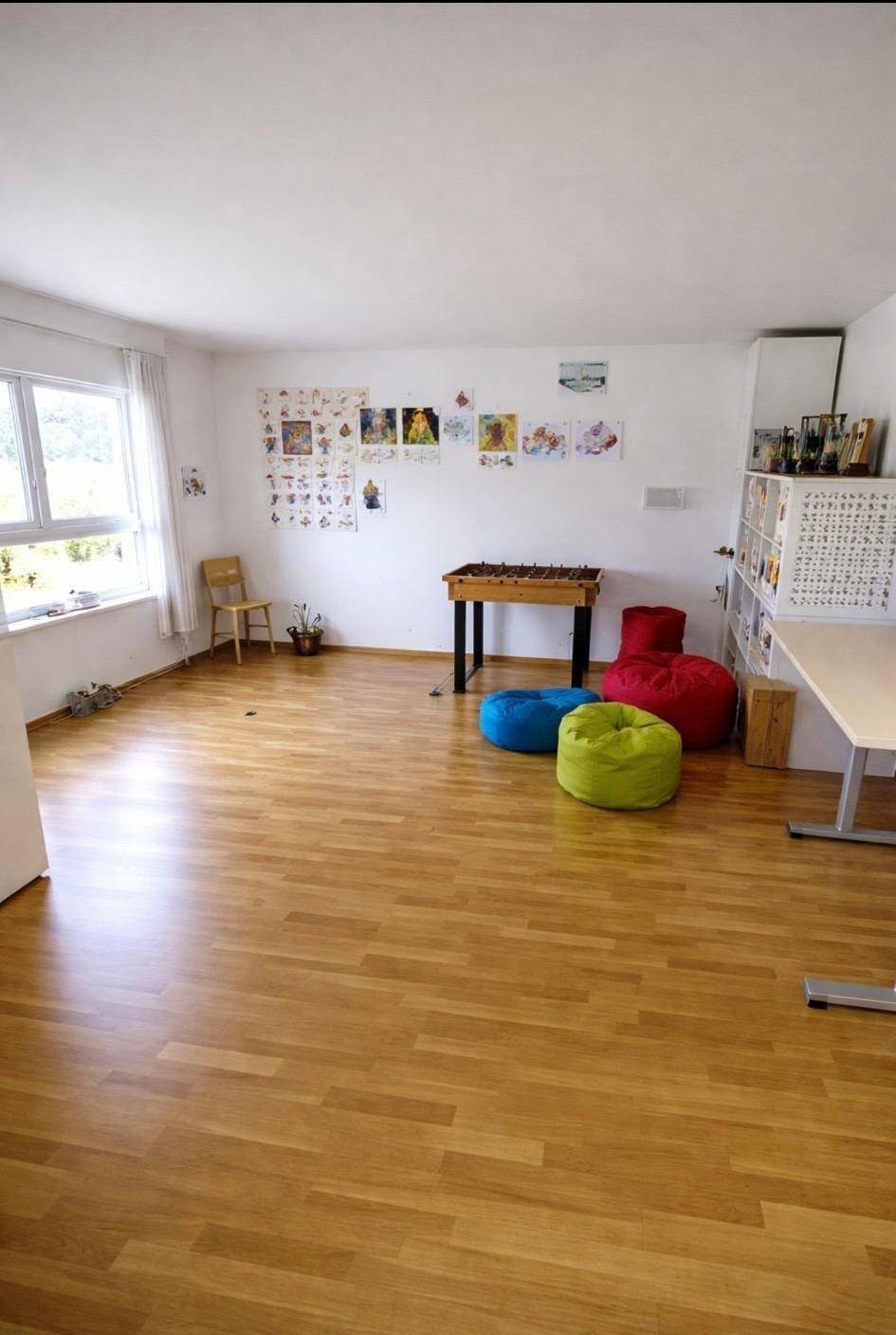 Geräumiges Zimmer mit Holzfußboden, bunten Sitzsäcken und viel Tageslicht.
