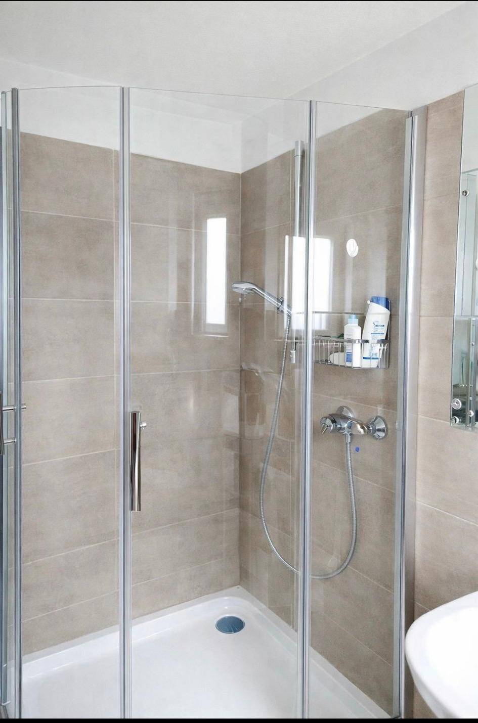 Modernes Badezimmer mit Duschkabine, beigen Fliesen und minimalistischem Design.