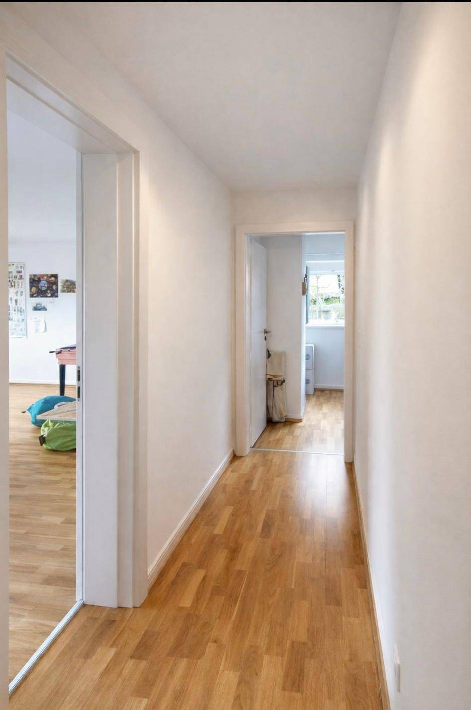 Heller Flur mit Holzfußboden, weißen Wänden und Zugang zu weiteren Räumen.