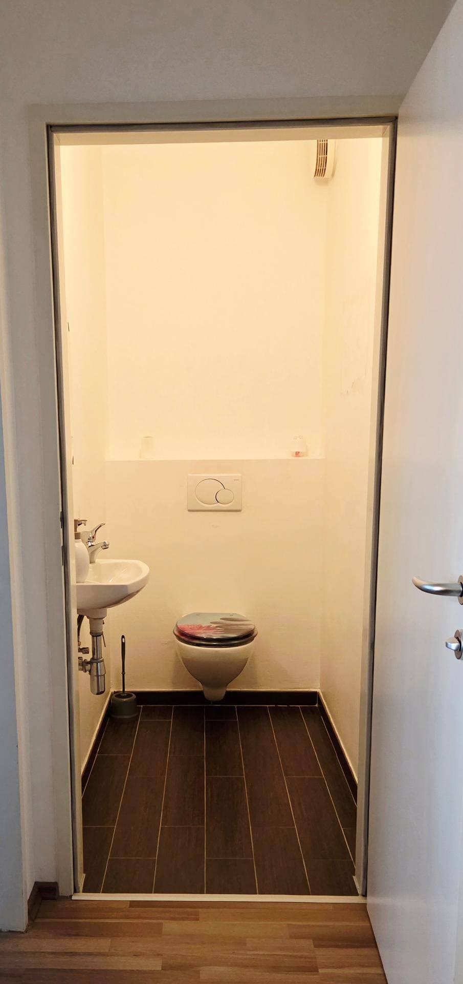 Separates Gäste-WC mit wandhängender Toilette und kleinem Handwaschbecken.
