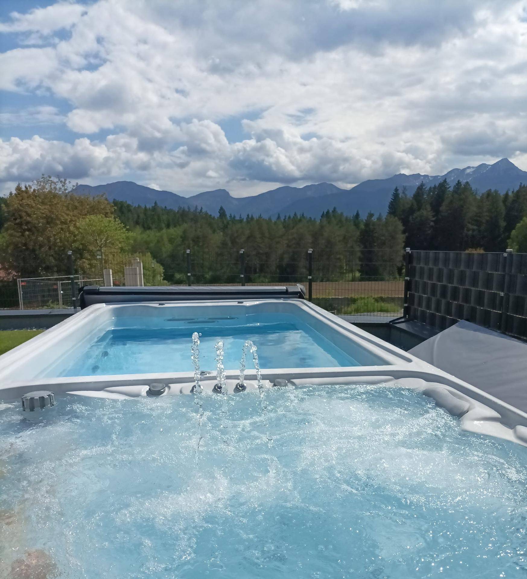 Außenbereich mit Whirlpool und Schwimmbecken, umgeben von Natur und mit Bergblick.