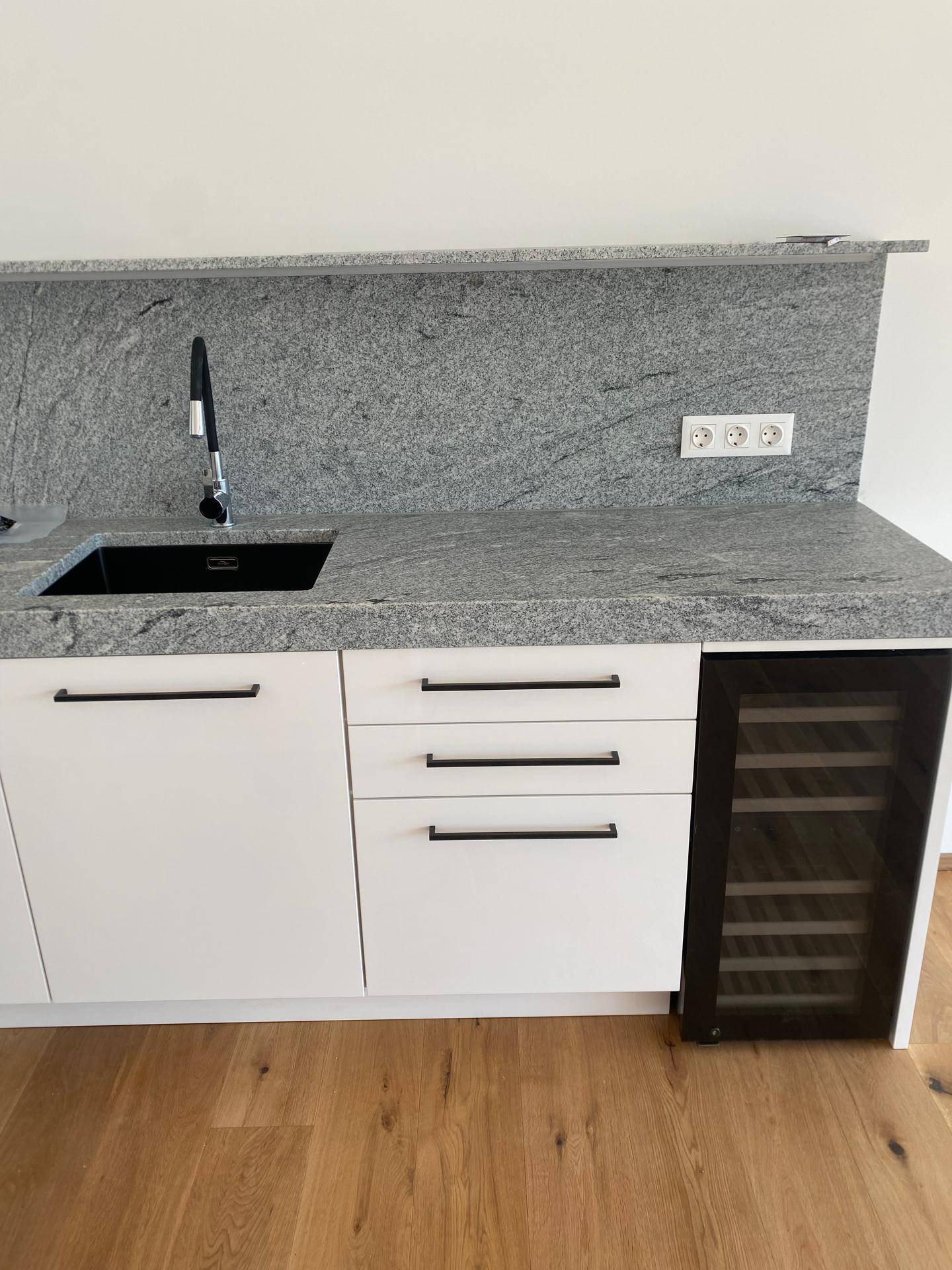 Küchenzeile mit Granitarbeitsplatte, schwarzem Spülbecken und integriertem Weinkühler.