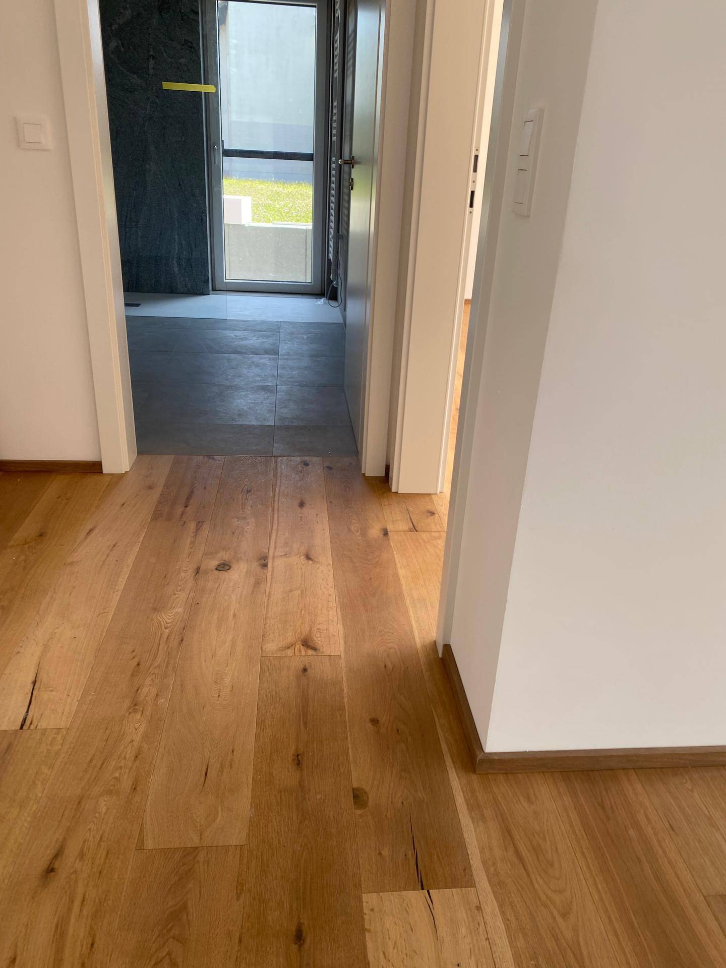 Heller Flur mit Holzboden, der zu weiteren Räumen und einem gefliesten Bereich führt.