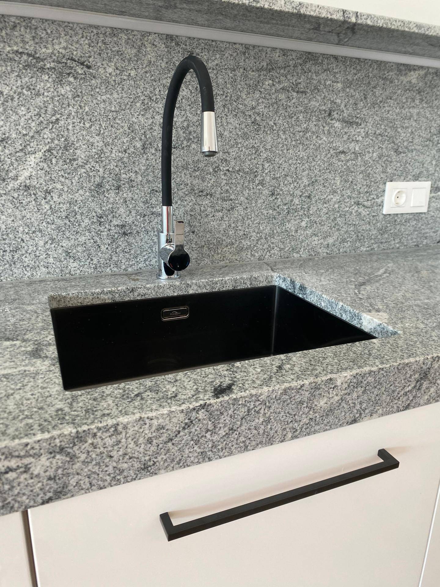 Nahaufnahme eines modernen schwarzen Spülbeckens mit flexiblem Wasserhahn in einer Granitarbeitsplatte.