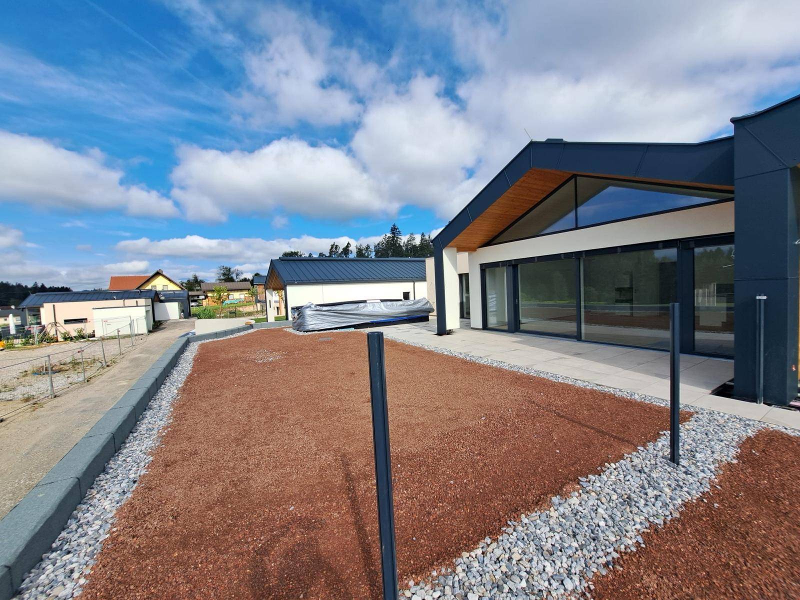 Außenansicht eines Neubaus mit moderner Architektur und vorbereitetem Gartenbereich unter blauem Himmel.