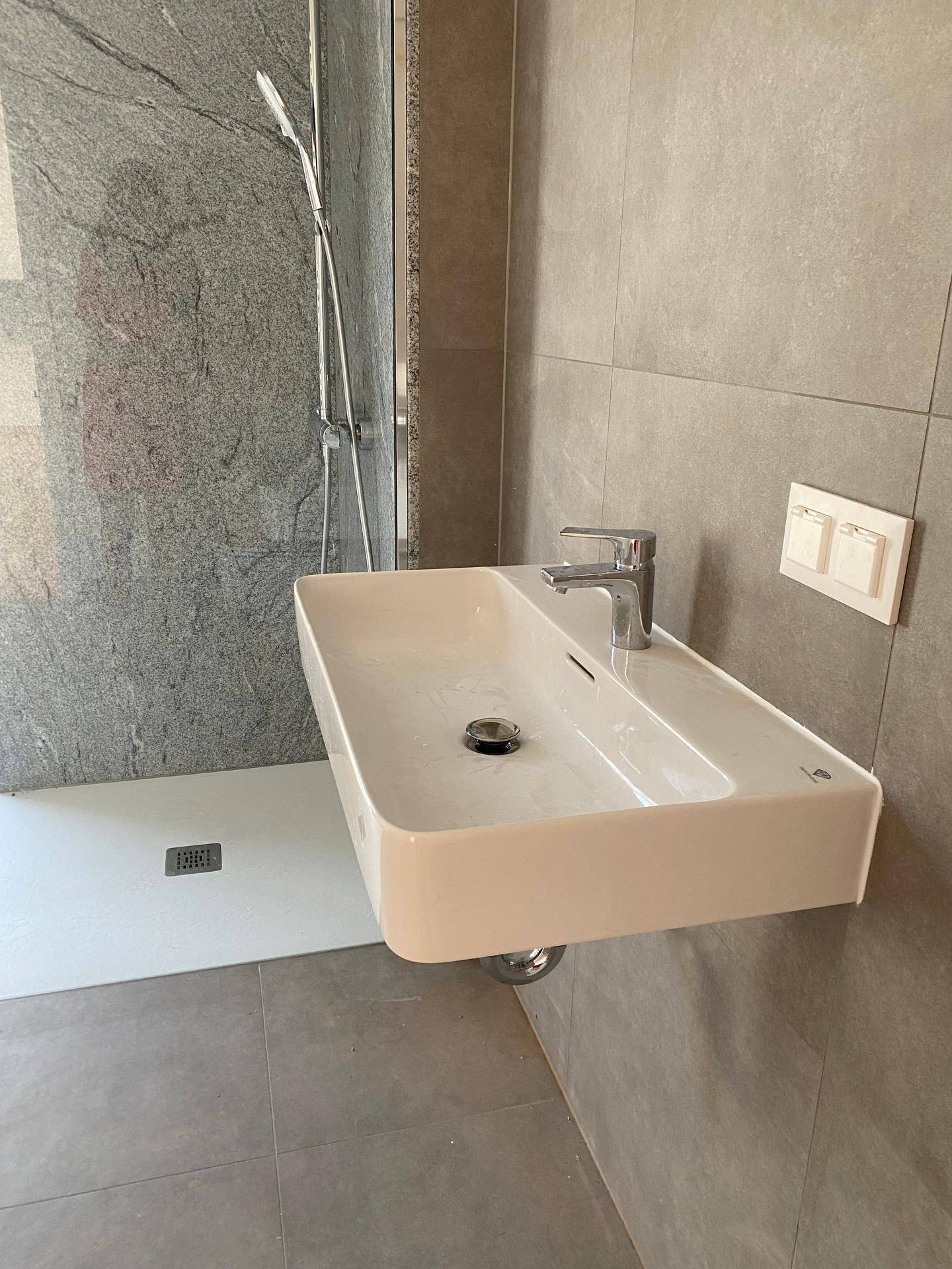 Modernes Waschbecken mit Armatur neben einer ebenerdigen Dusche in einem gefliesten Badezimmer.