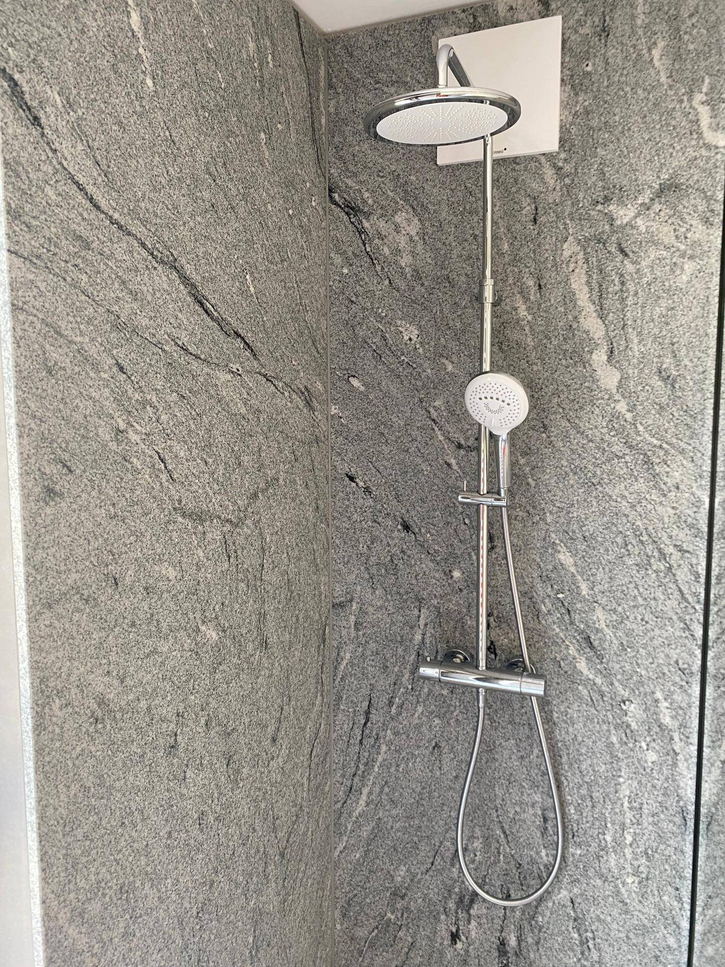 Nahaufnahme einer modernen Regendusche mit großem Duschkopf in einem gefliesten Duschbereich.
