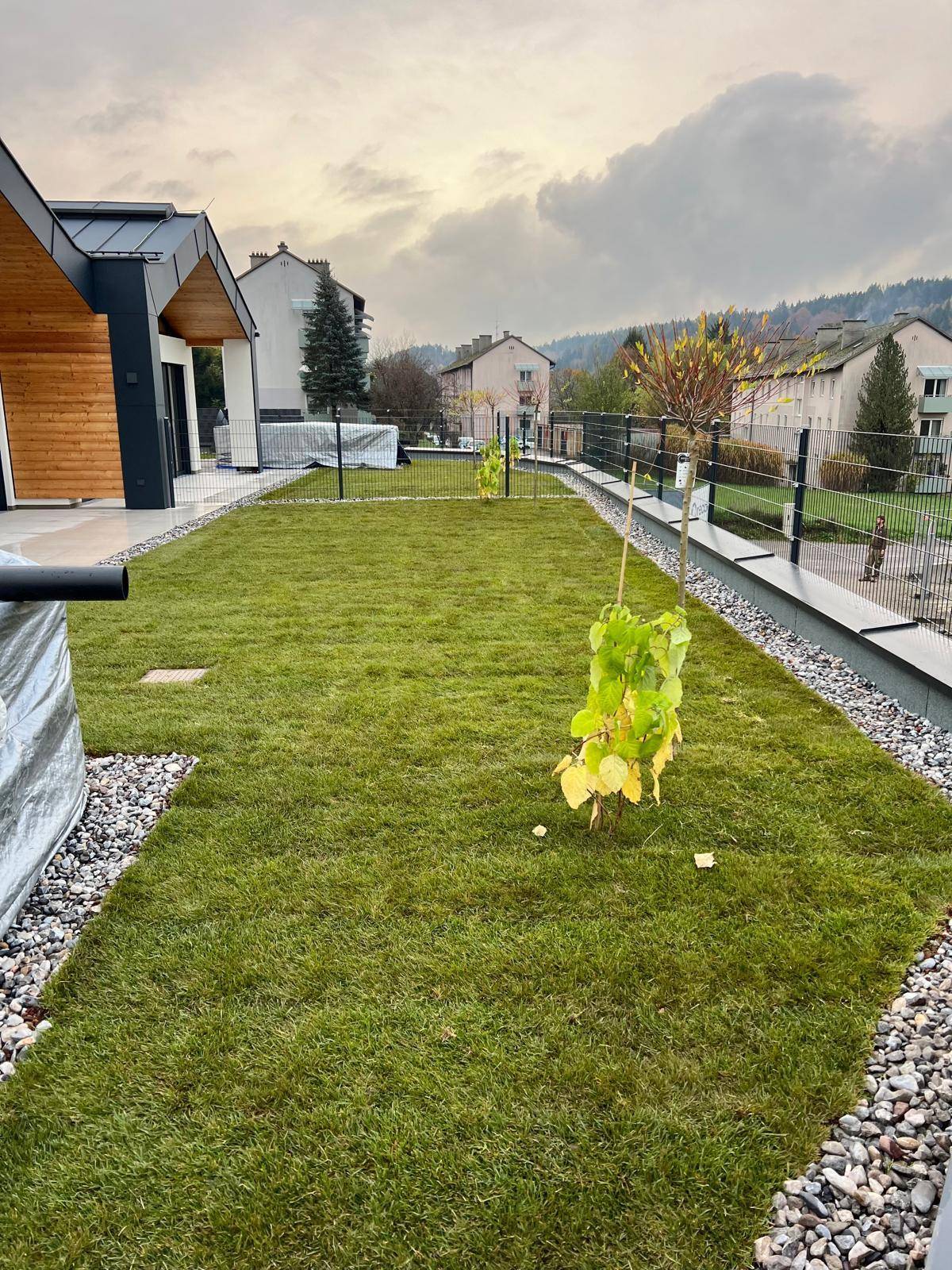 Neu angelegter Gartenbereich mit frischem Rasen und jungen Pflanzen, umgeben von einer modernen Einfriedung.