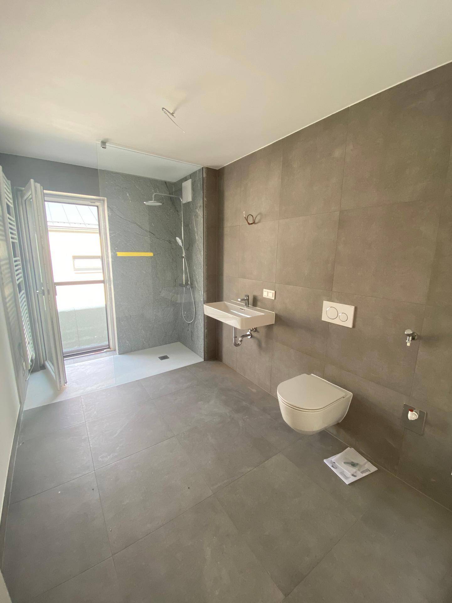 Modernes Badezimmer mit grauen Fliesen, ebenerdiger Dusche und wandhängendem WC.