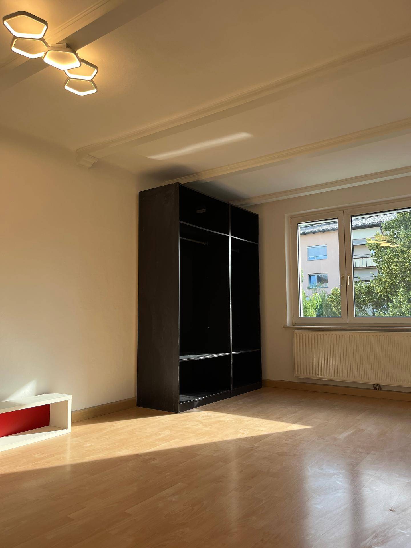 Helles Zimmer mit Holzfußboden, einem offenen Kleiderschrank und einem großen Fenster.