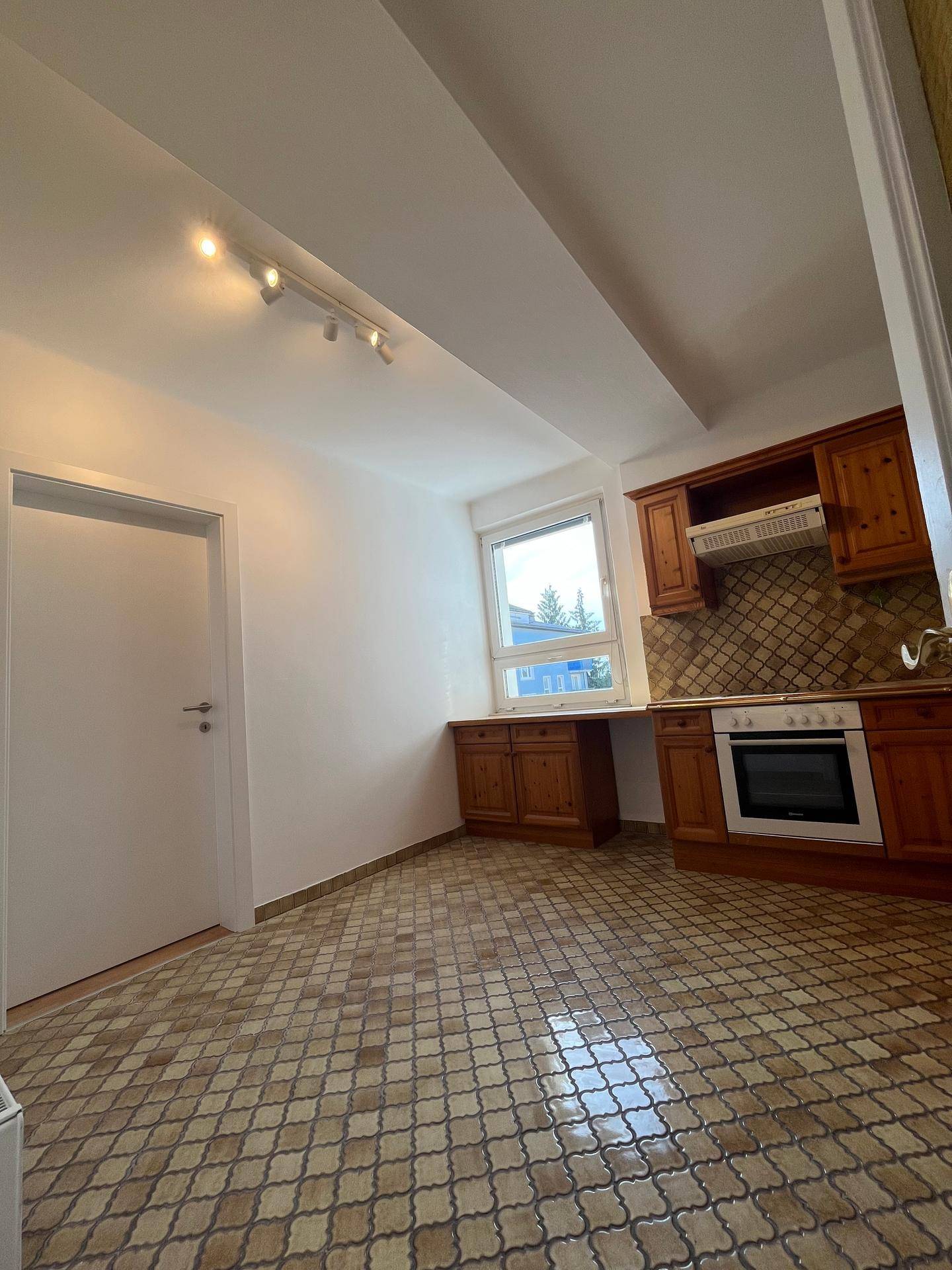 Funktionale Küche mit Holzmöbeln, gemustertem Fliesenboden und einem Fenster für Tageslicht.