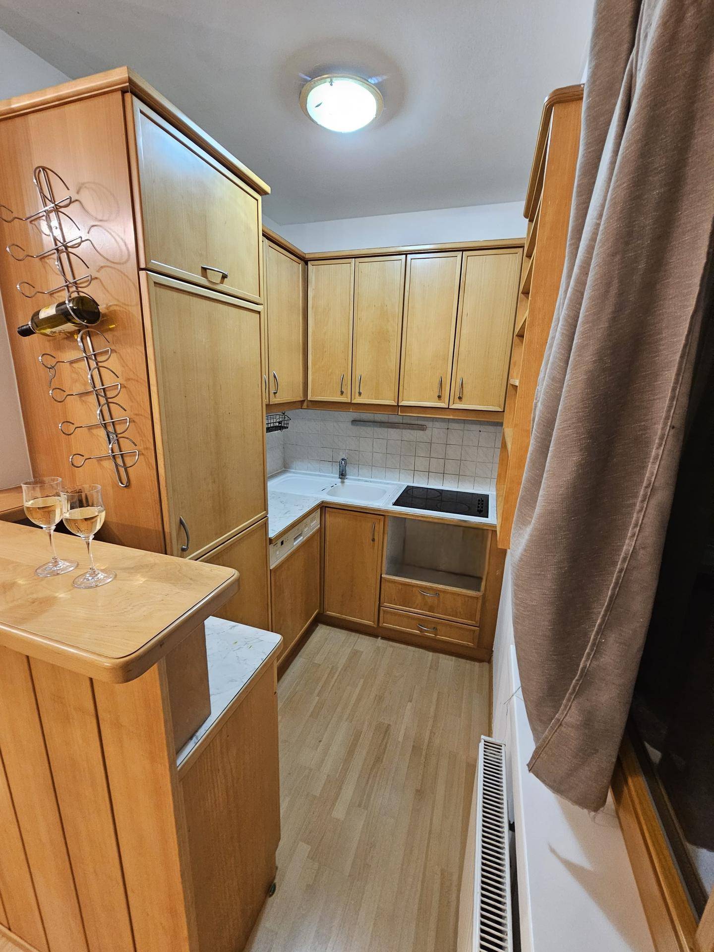 Funktionale Küche mit Holzmöbeln, Kochfeld und Fenster für natürliches Licht.