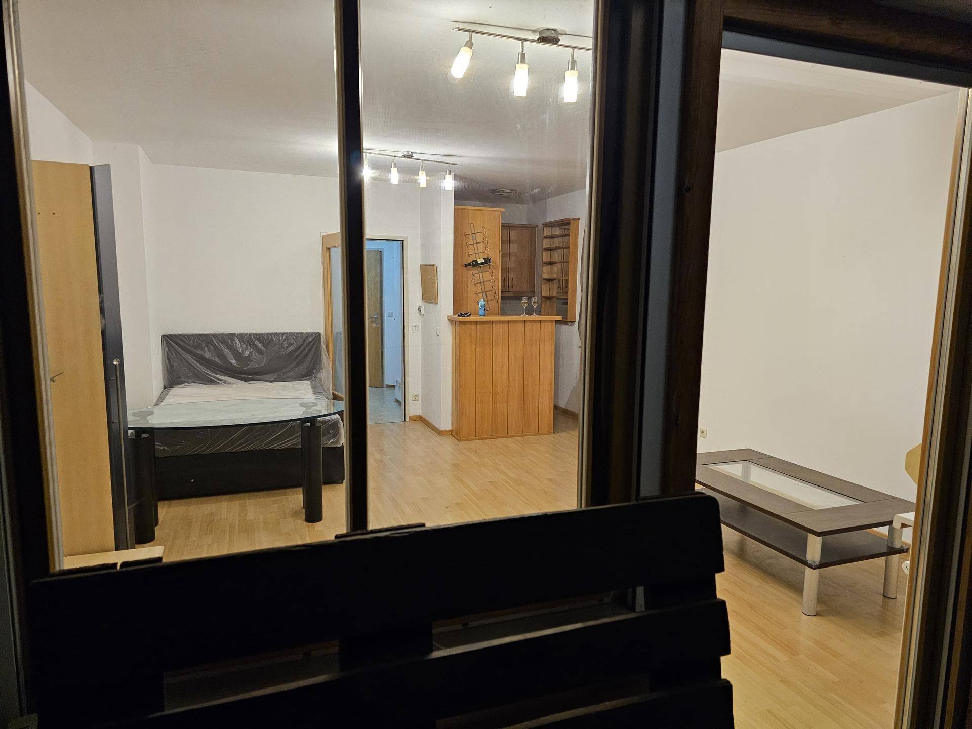 Blick vom Balkon in den hellen Wohnbereich mit Holzboden und integrierter Küchenzeile.