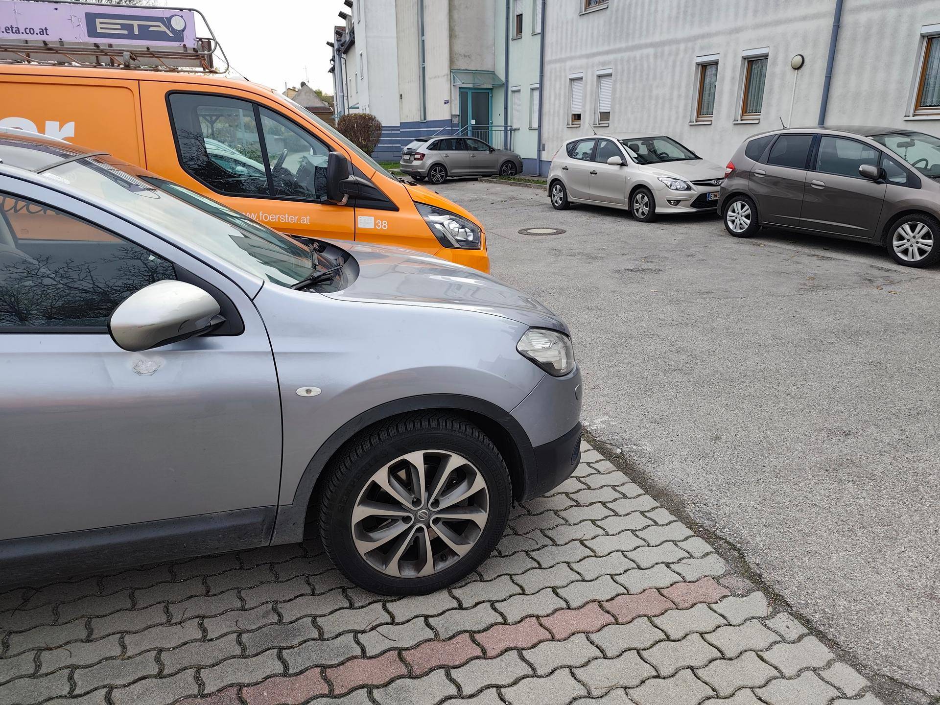 Außenparkplätze auf gepflastertem Gelände vor einem Wohngebäude.