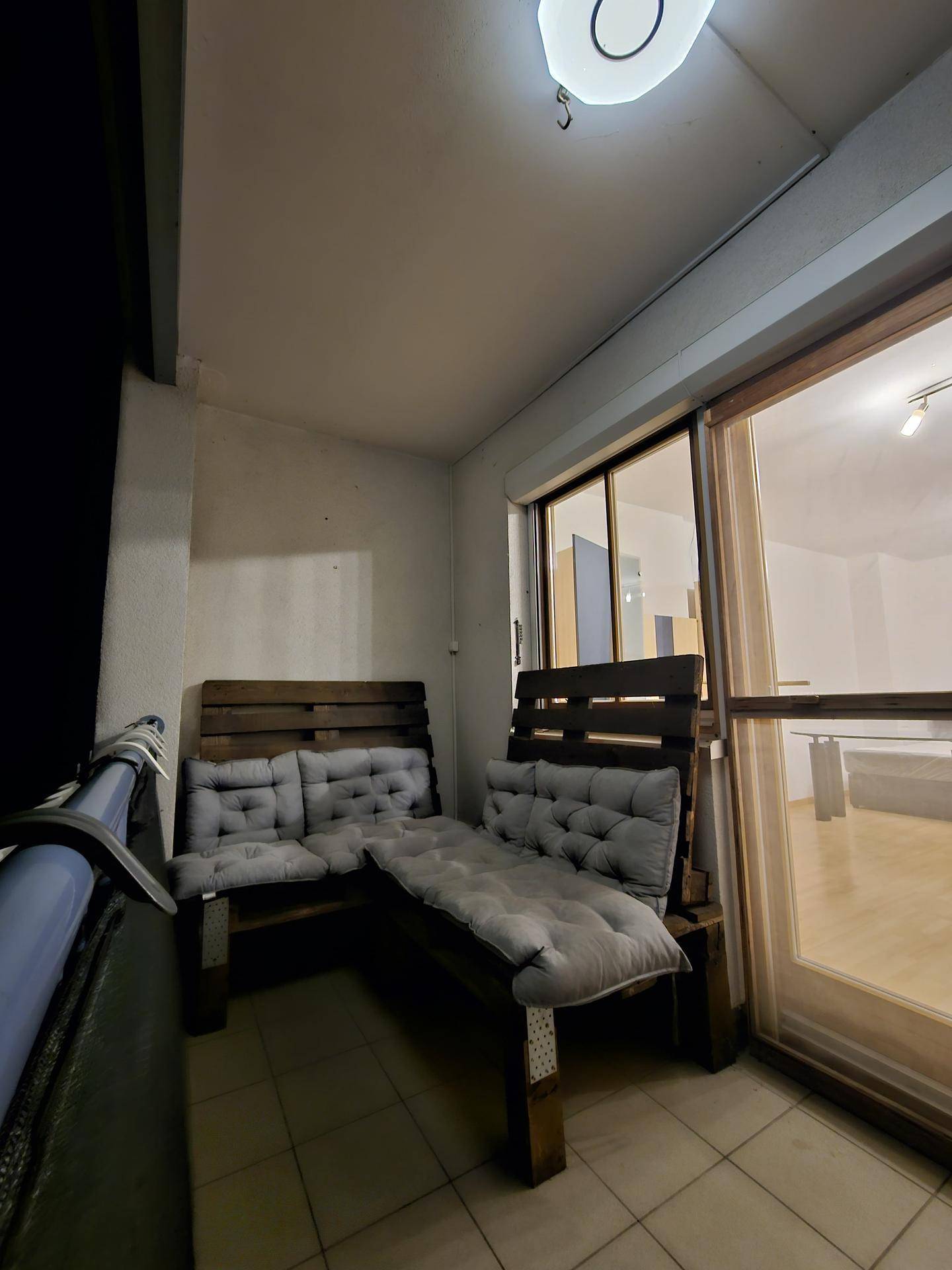 Balkon bei Nacht mit Sitzgelegenheiten und Blick in den beleuchteten Wohnbereich.