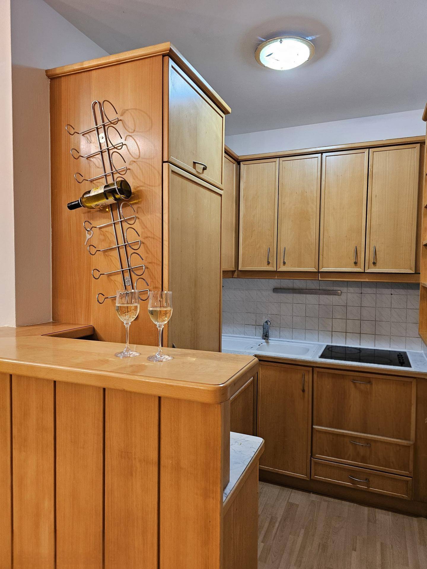 Kleine Küche mit Holzschränken, integriertem Weinflaschenregal und einer Frühstücksbar.