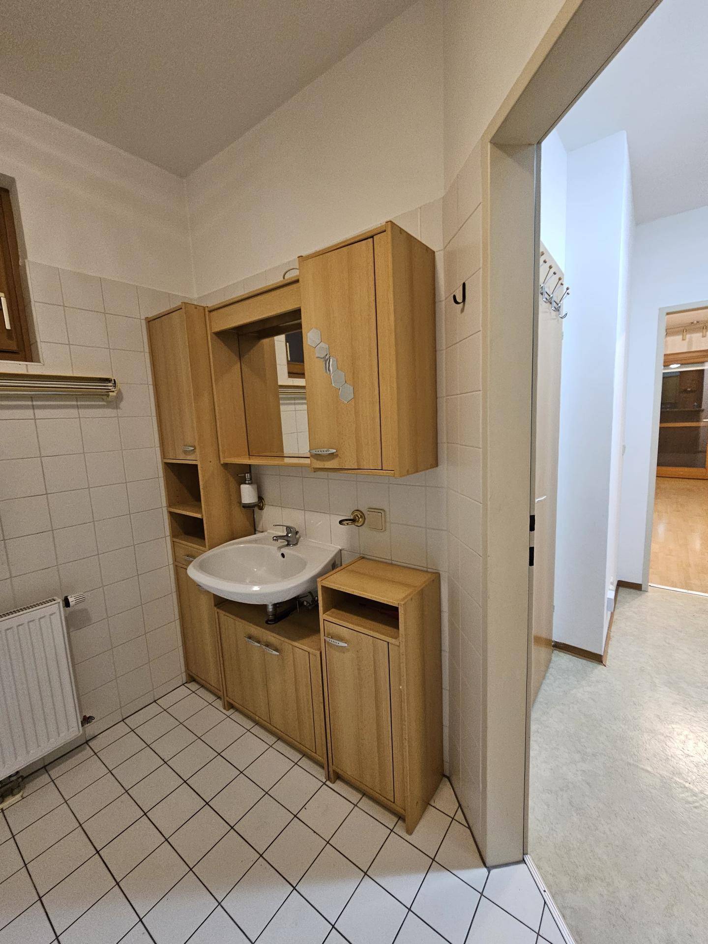 Badezimmer mit Waschbecken, Spiegelschrank und Zugang zum Flur.