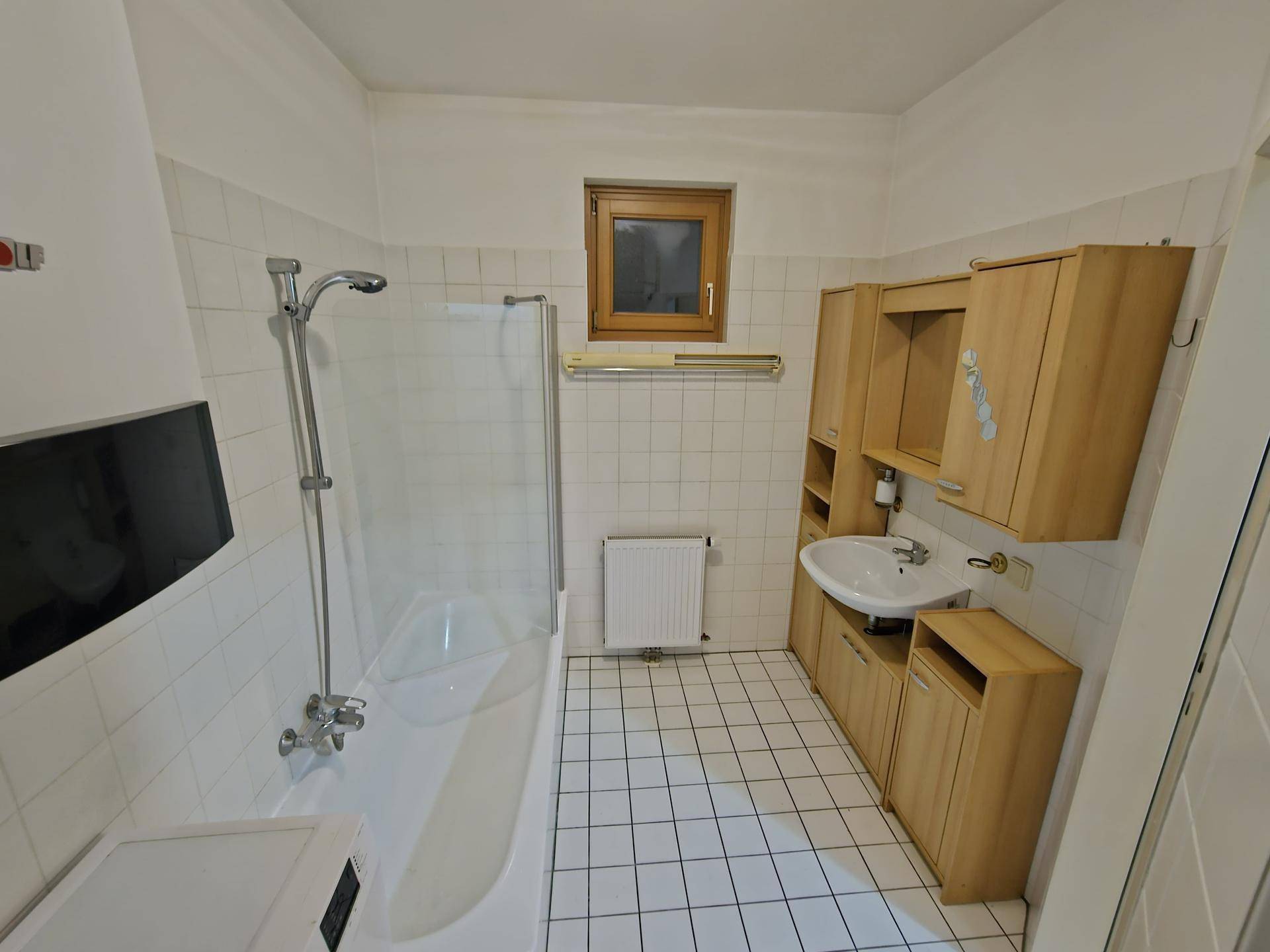 Badezimmer mit Badewanne, Duschvorrichtung, Waschbecken und Holzschränken.