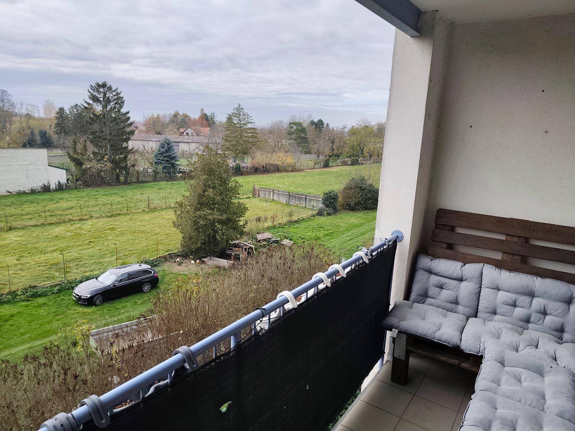 Balkon mit Sitzgelegenheiten und weitem Blick auf grüne Felder unter bewölktem Himmel.