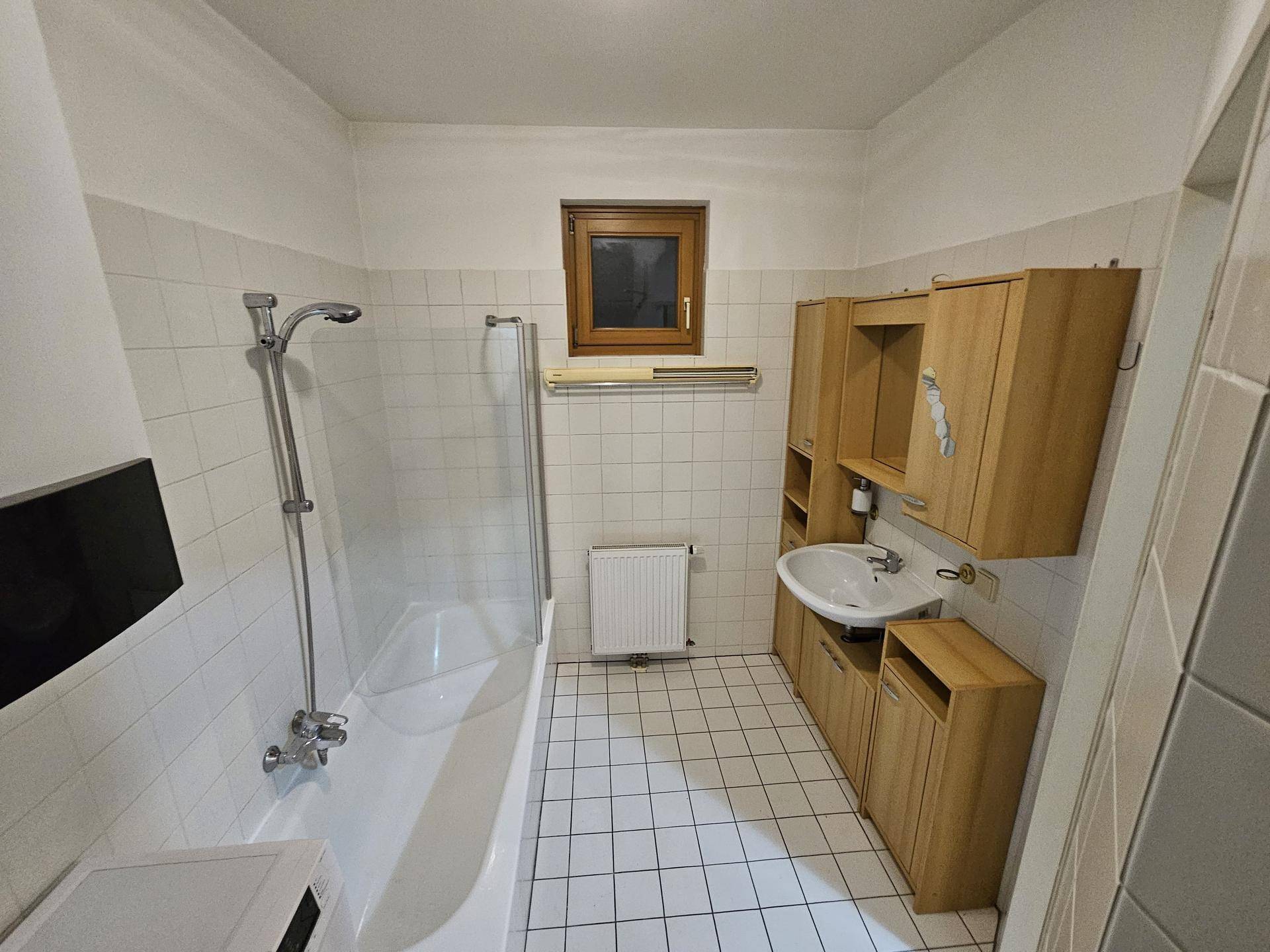 Helles Badezimmer mit Badewanne, Duschvorrichtung und praktischen Holzmöbeln.