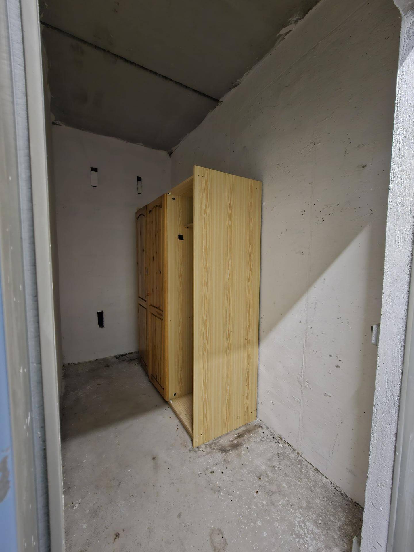 Abstellraum im Kellerbereich mit unfertigen Wänden und einem Holzschrank.