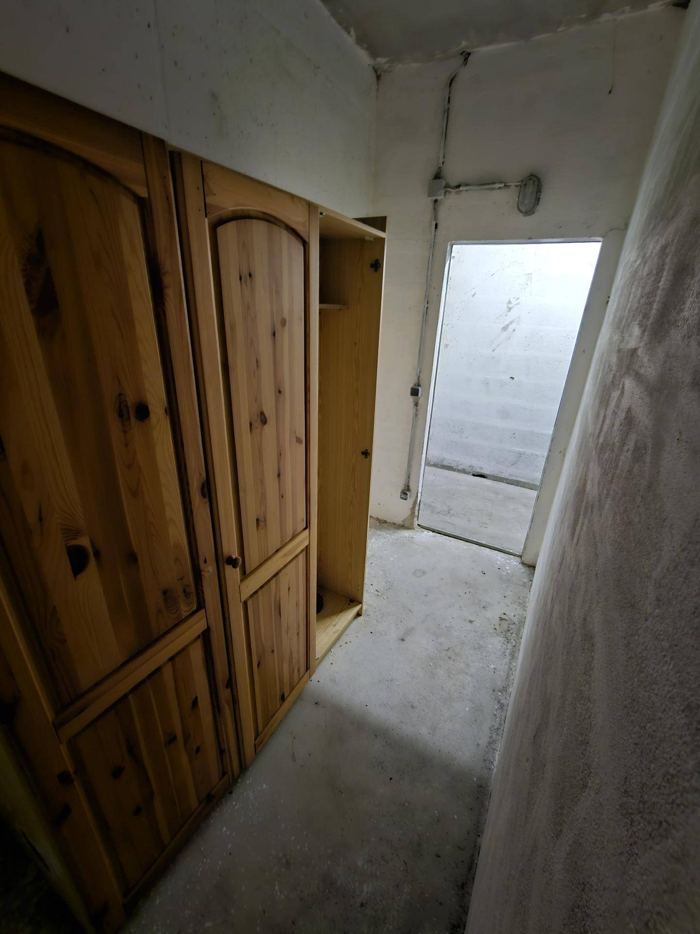 Kellerabteil mit Holzschrank und Blick auf einen weiteren Raum oder Ausgang.