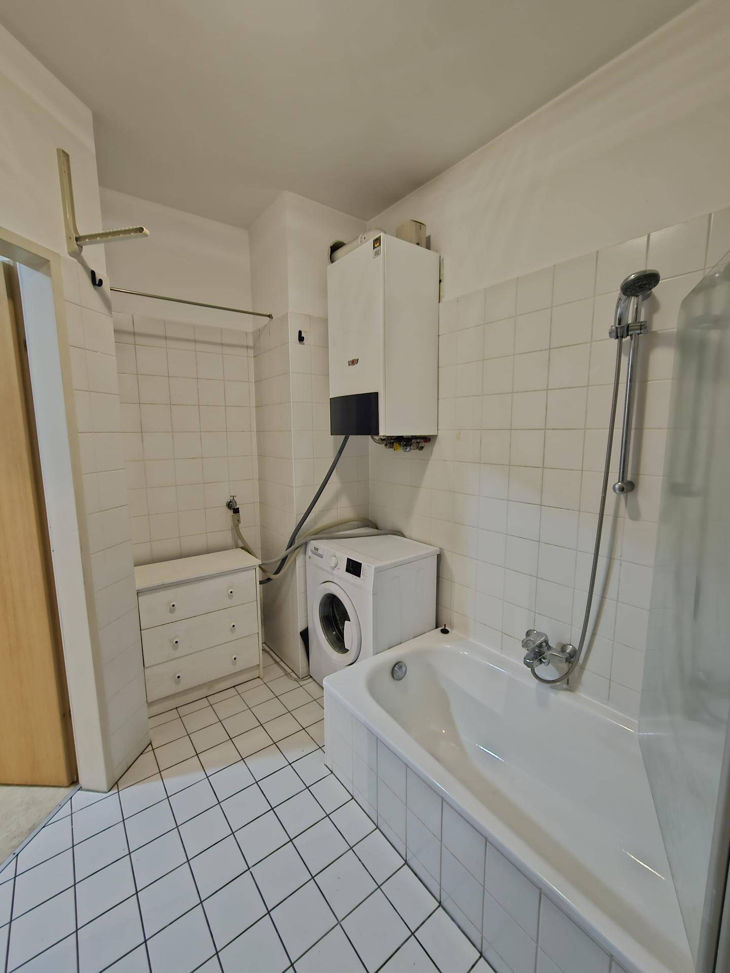 Badezimmer mit Badewanne, Waschmaschine und Warmwasserbereiter, funktional eingerichtet.
