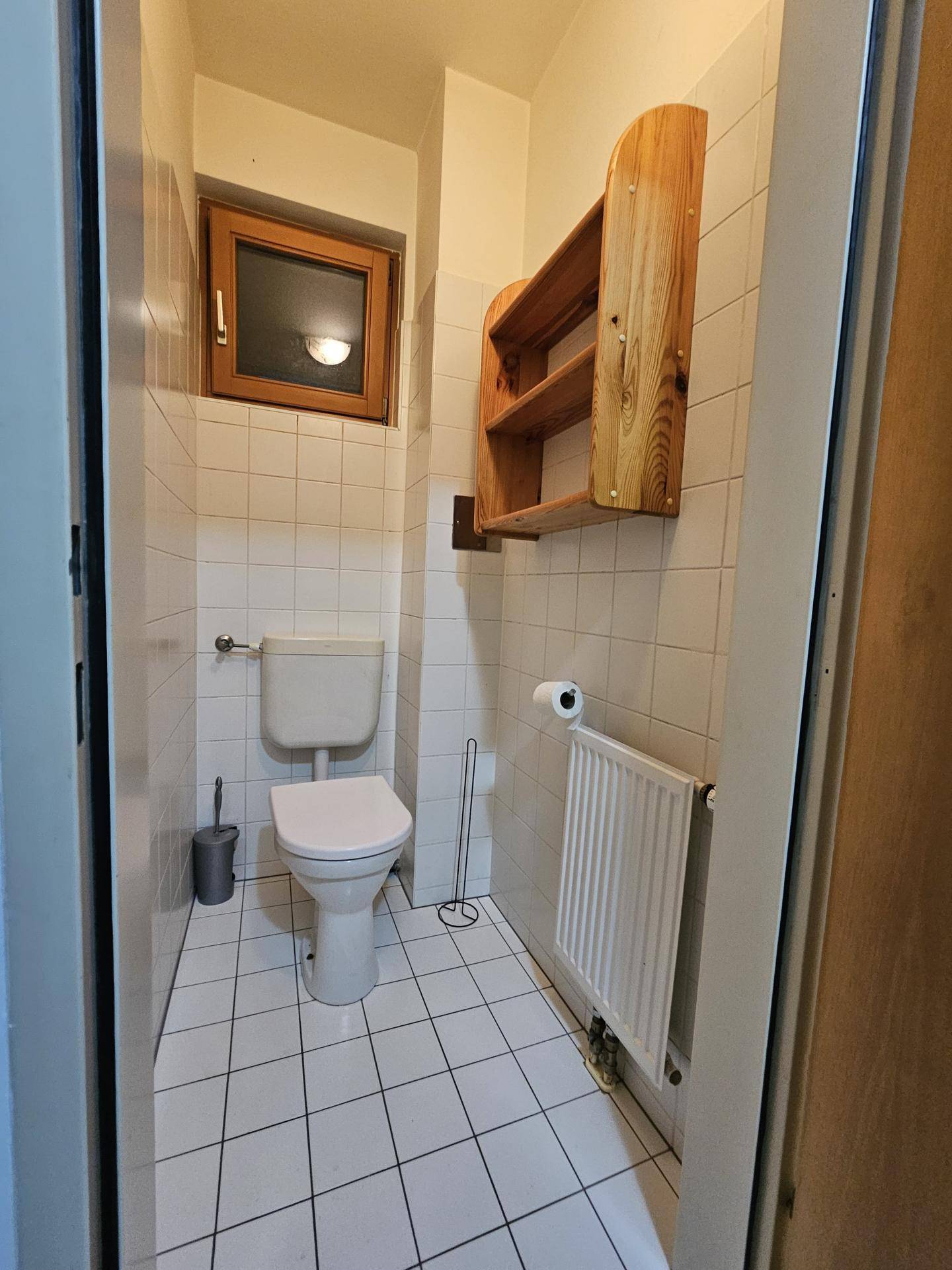Separates WC mit Toilette, Fenster und einem kleinen Holzregal für Utensilien.