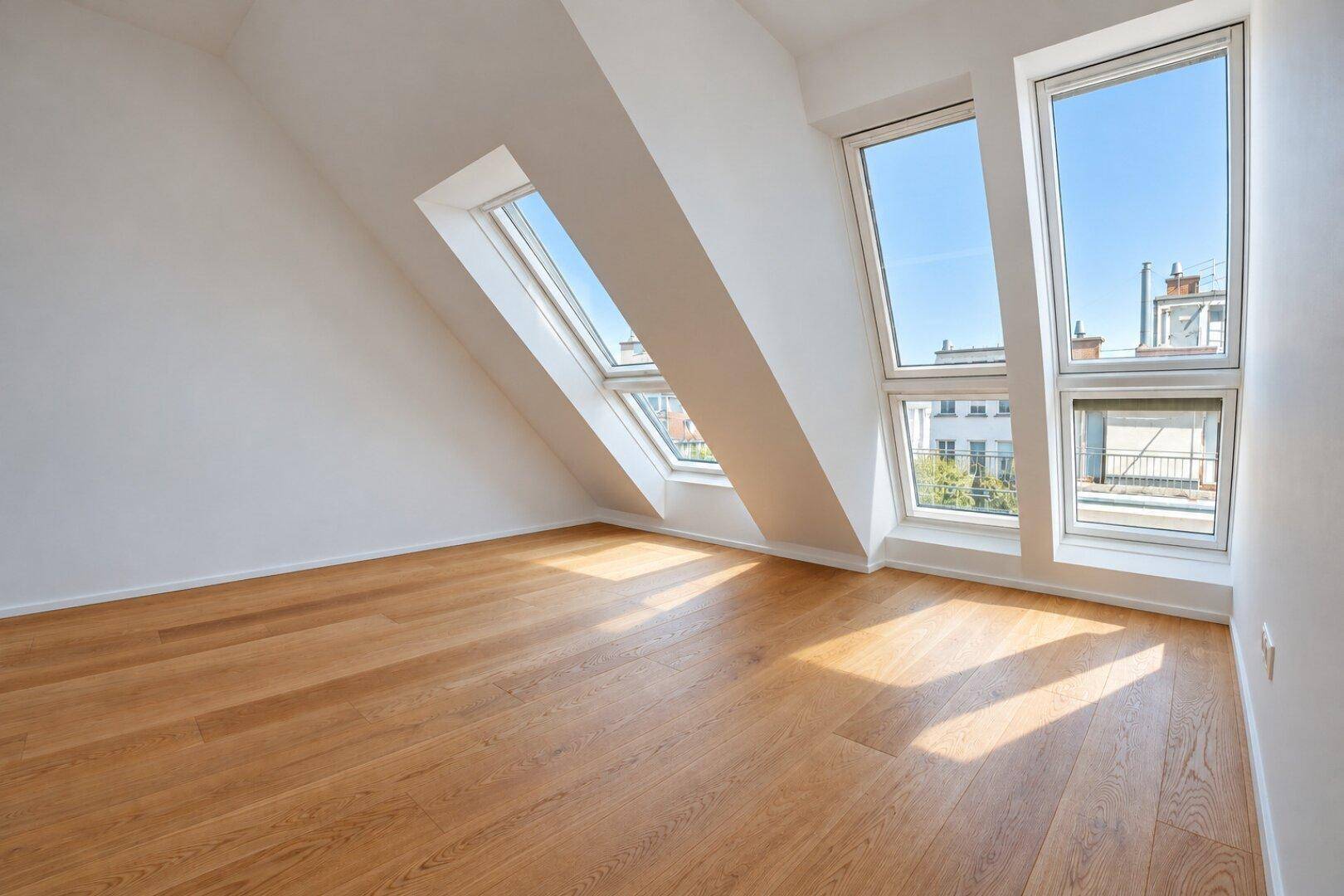 Heller Raum im Dachgeschoss mit schrägen Wänden und großen Dachfenstern.