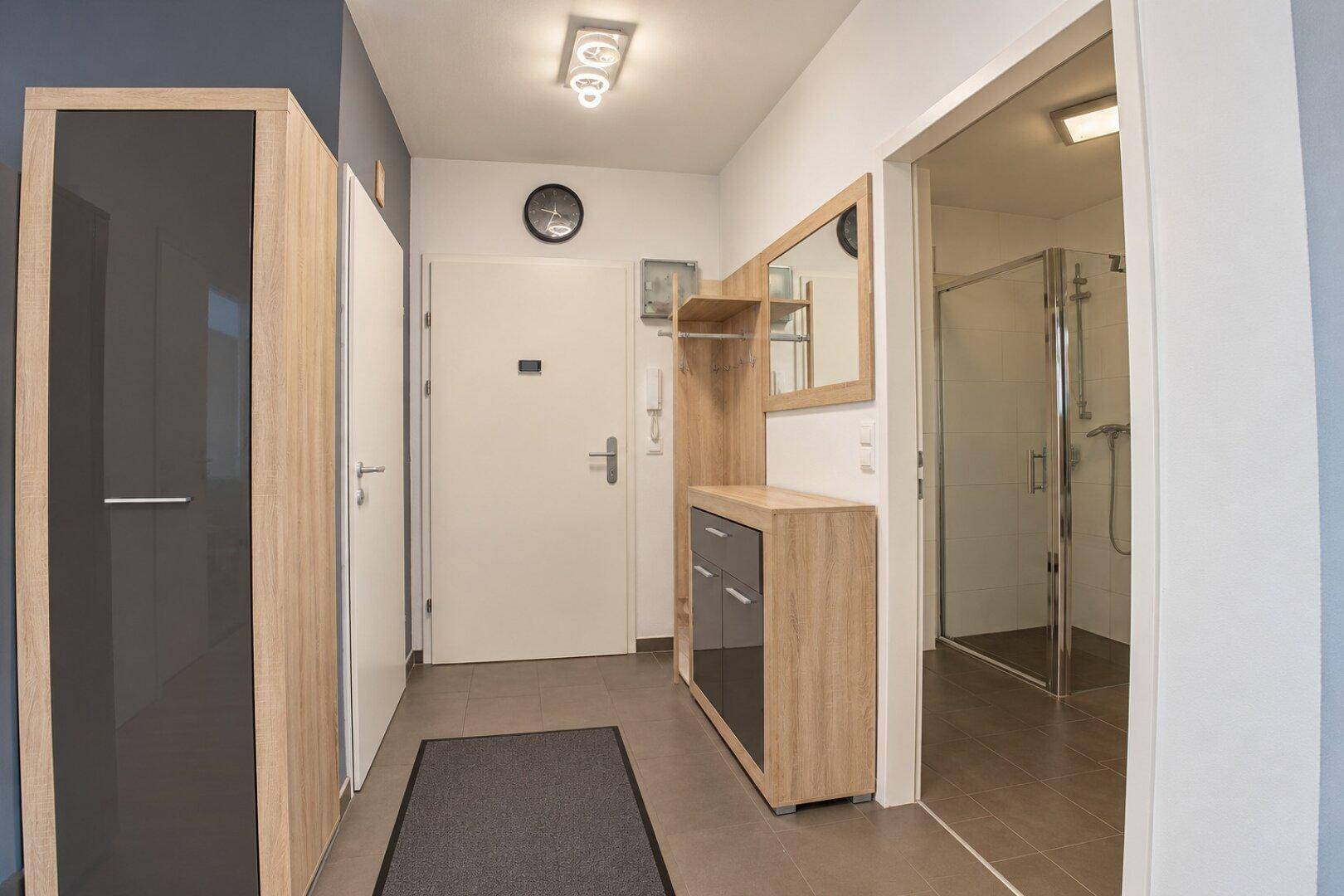 Heller Eingangsbereich mit Garderobe, Spiegel und Zugang zum Badezimmer.