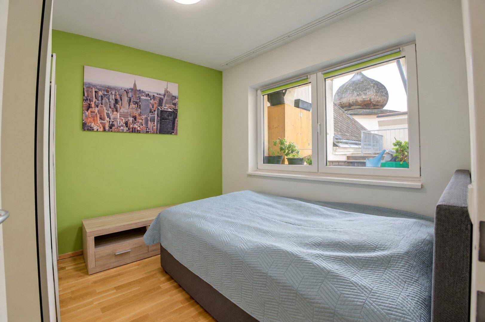 Schlafzimmer mit grüner Akzentwand, Einzelbett und Blick auf ein historisches Dach.