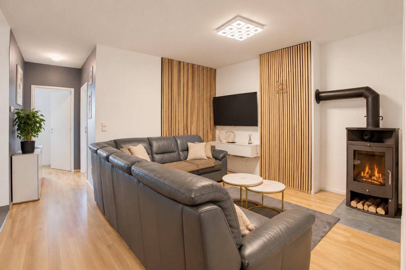 Gemütliches Wohnzimmer mit Kaminofen, großem Sofa und Holzakzenten an der Wand.