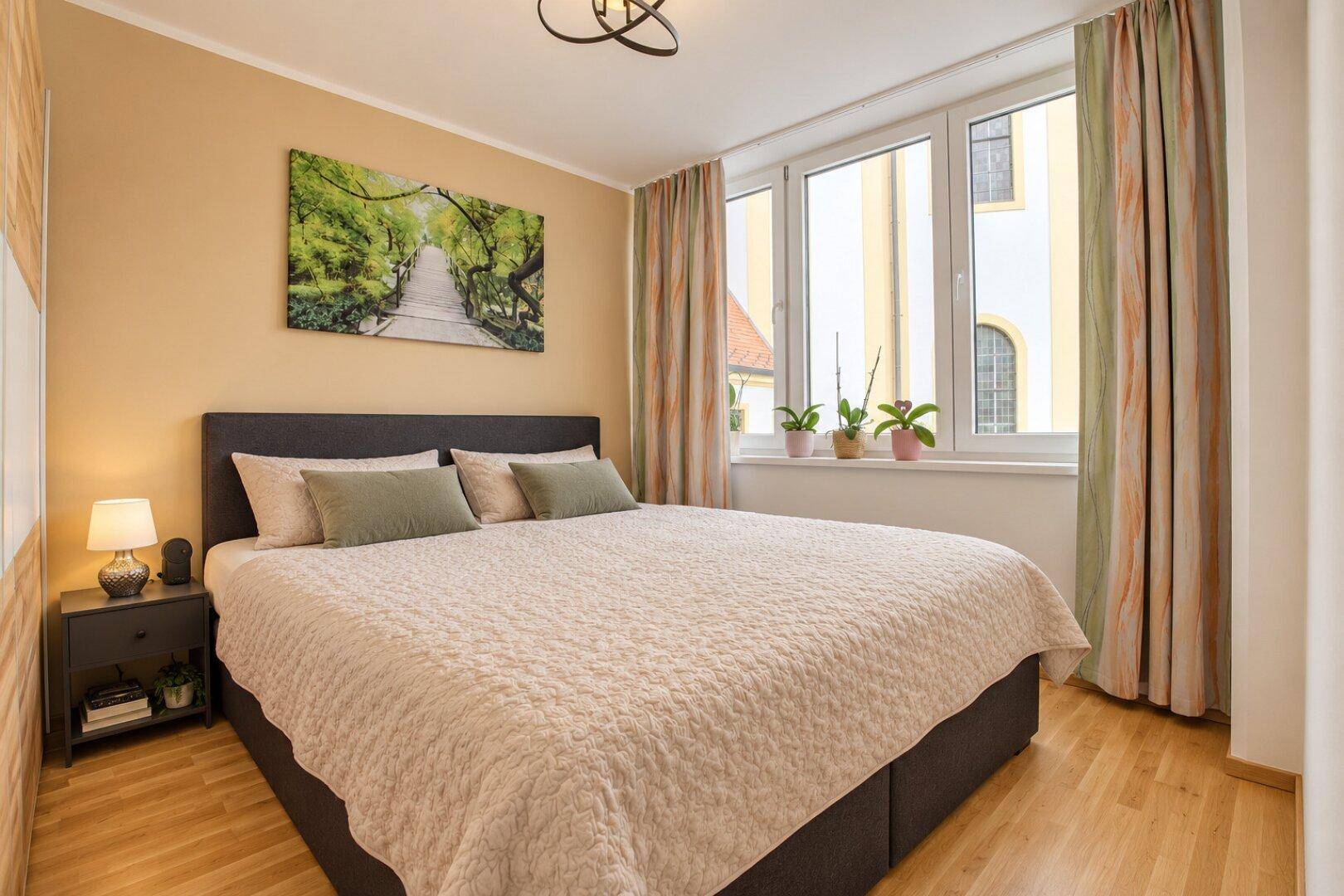 Helles Schlafzimmer mit Doppelbett, Holzboden und Blick auf ein Kirchengebäude.
