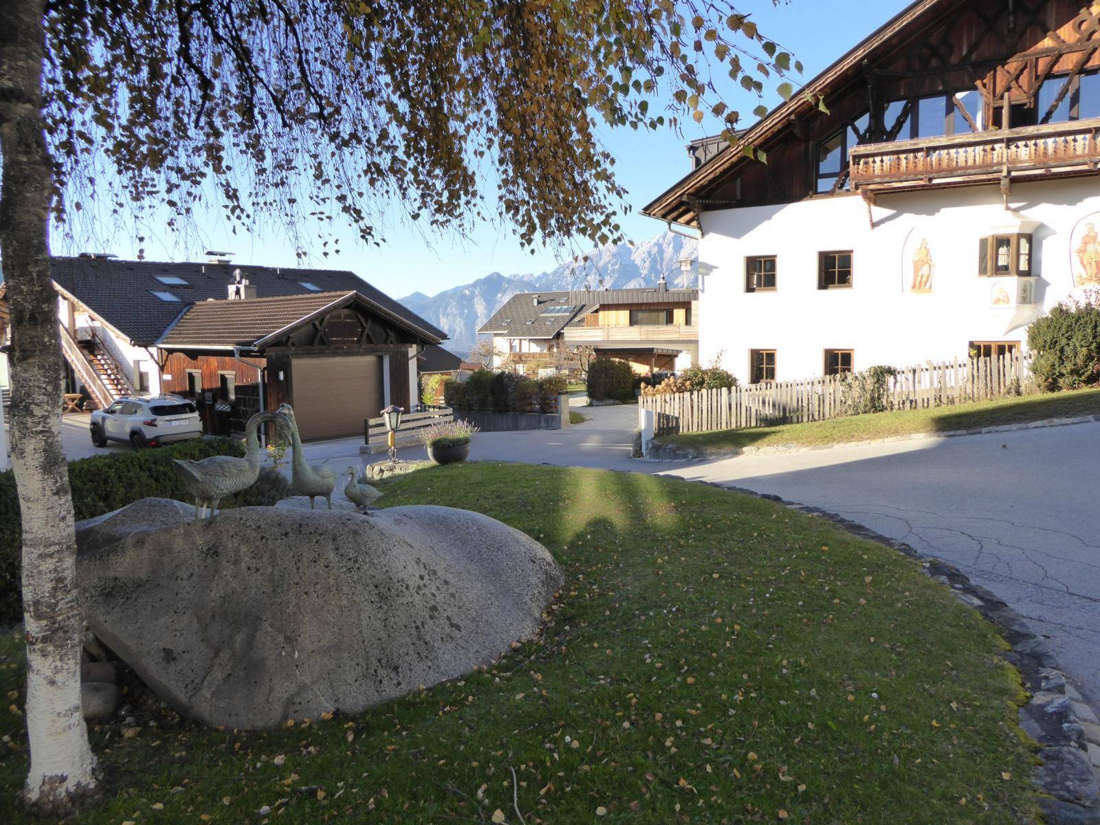 Dorfstraße mit traditionellen Häusern, gepflegtem Rasen und beeindruckendem Bergblick im Hintergrund.