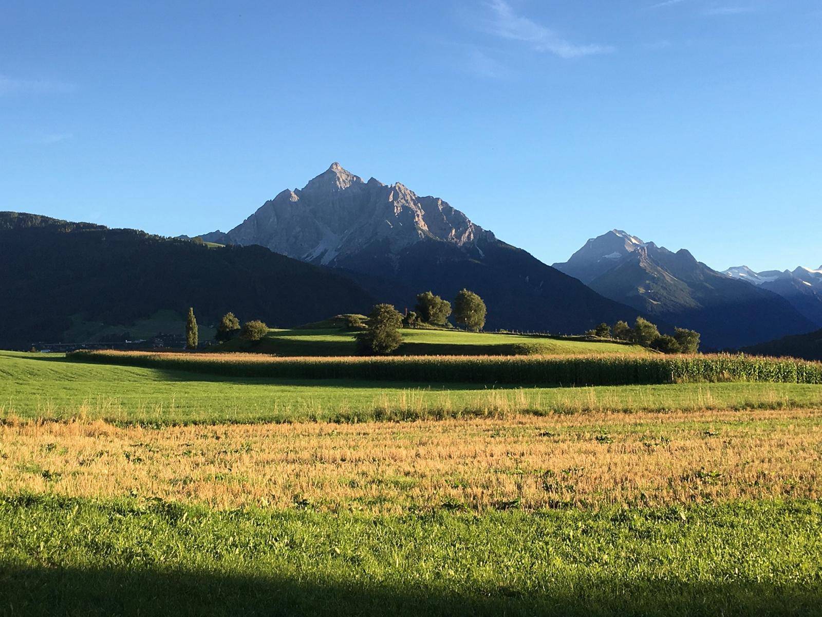 Malerische Landschaft mit weiten Feldern und imposanten Bergen unter einem strahlend blauen Himmel.