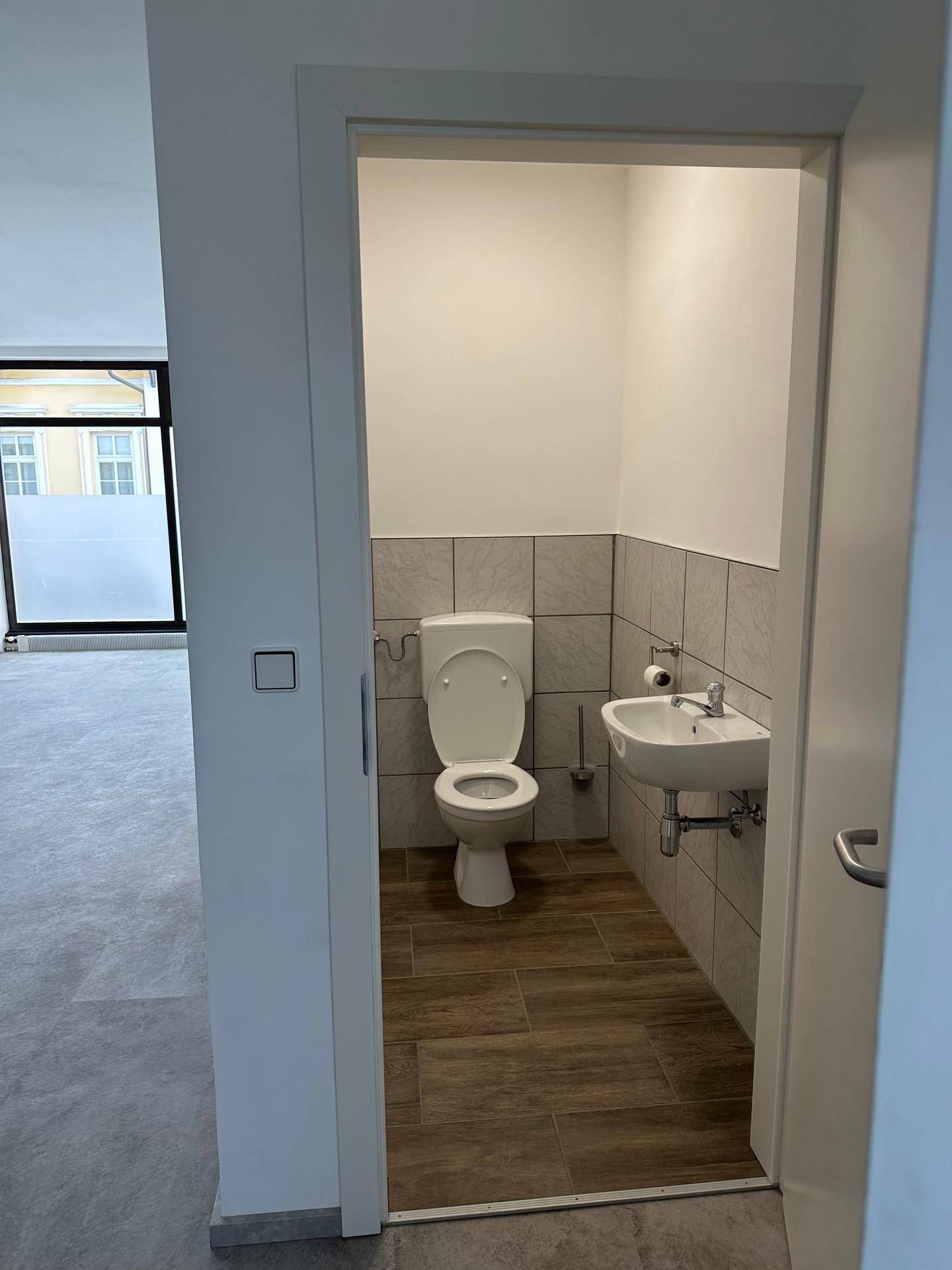 Kleines Gäste-WC mit modernen Fliesen, weißer Toilette und Waschbecken, vom Hauptraum aus zugänglich.