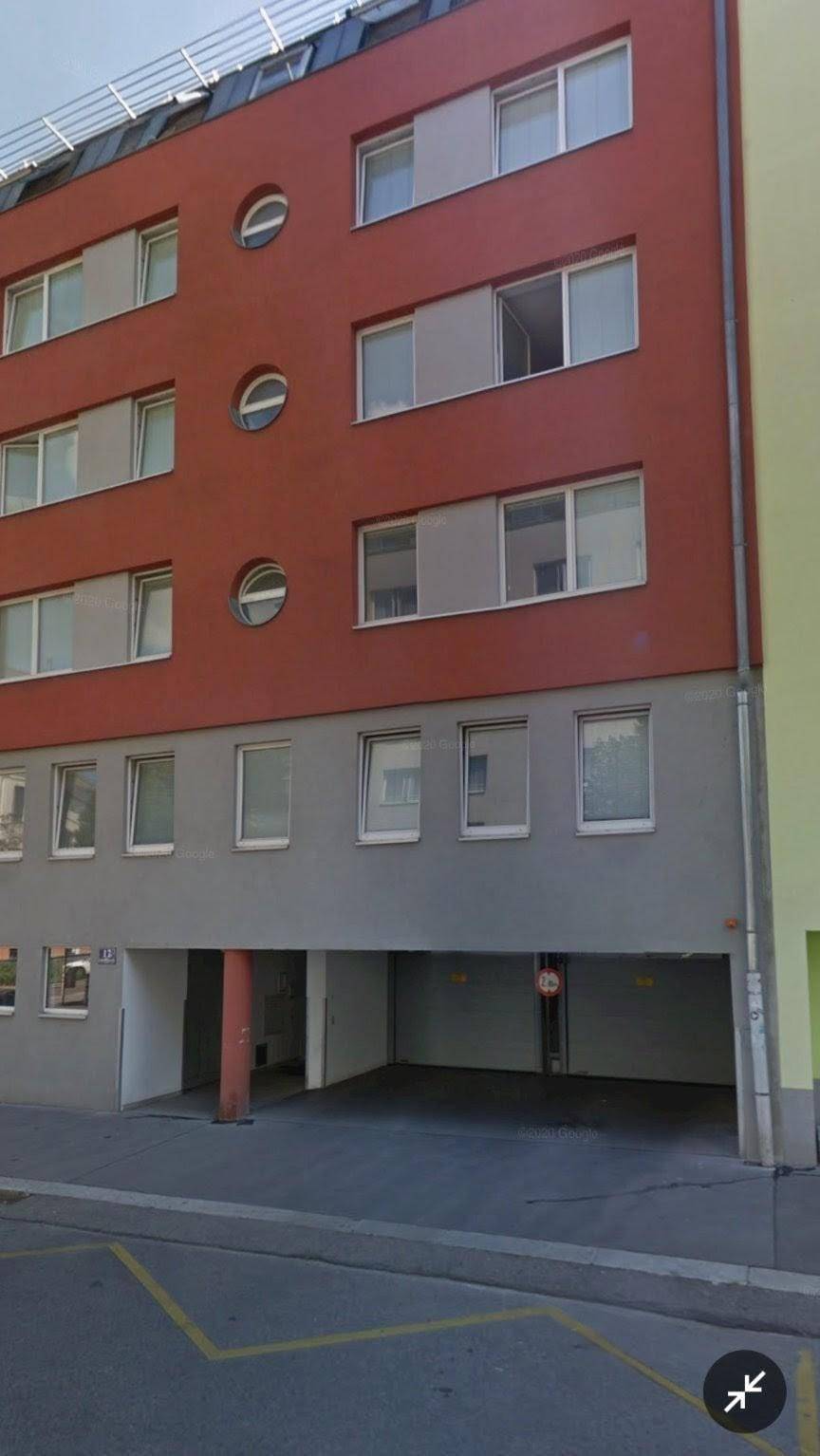 Nahaufnahme der roten Gebäudefassade mit offenem Parkbereich im Erdgeschoss.
