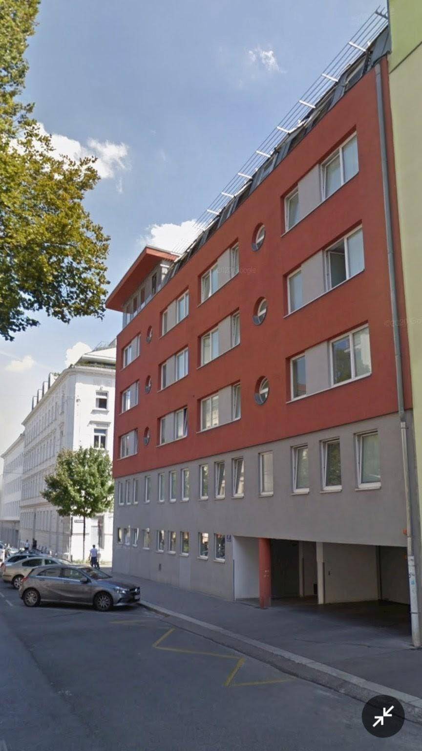 Moderne Wohnfassade in Rot mit zahlreichen Fenstern und Solaranlage auf dem Dach.