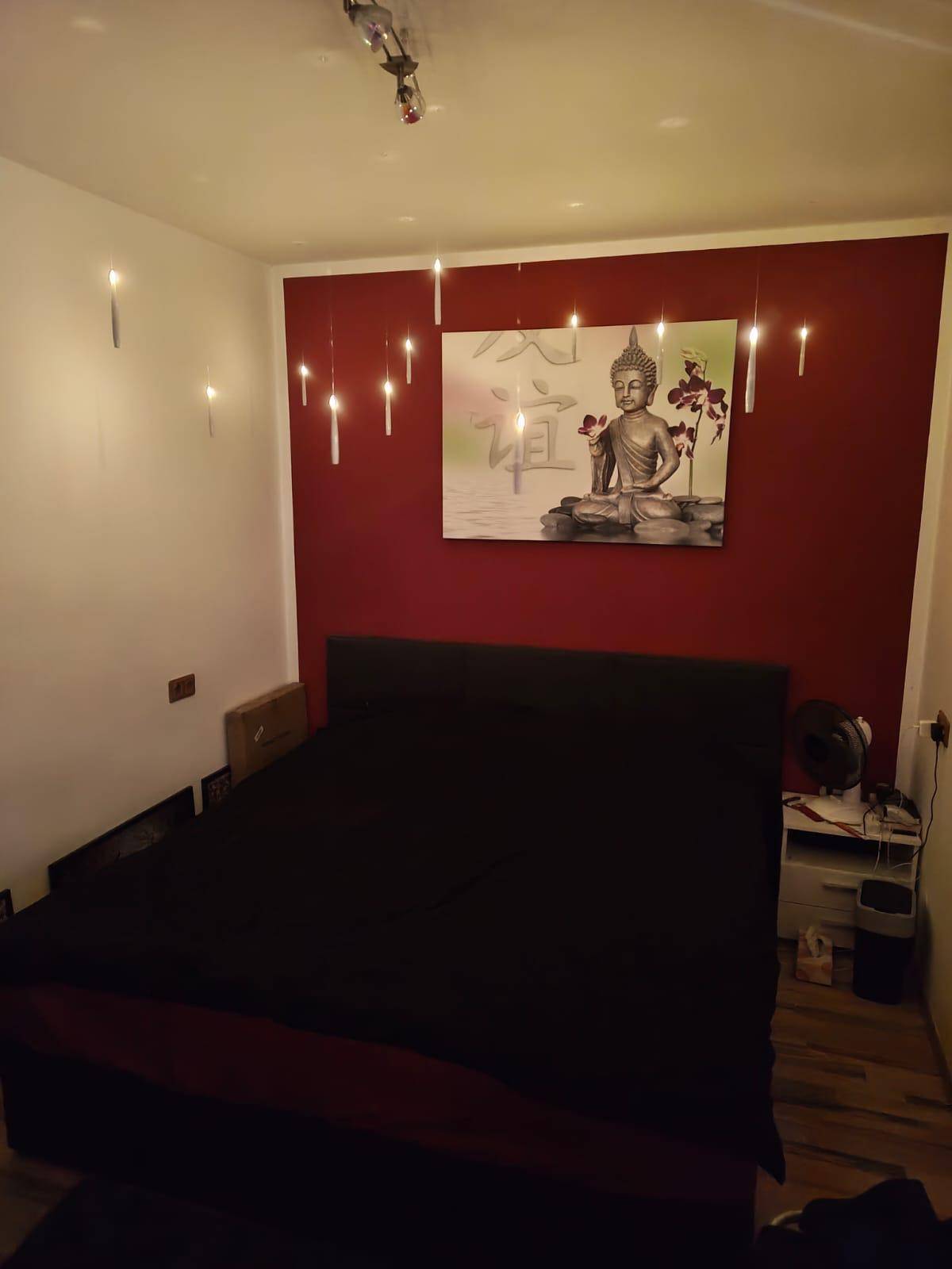 Schlafzimmer mit dunklem Doppelbett, roter Akzentwand und indirekter Beleuchtung für Atmosphäre.